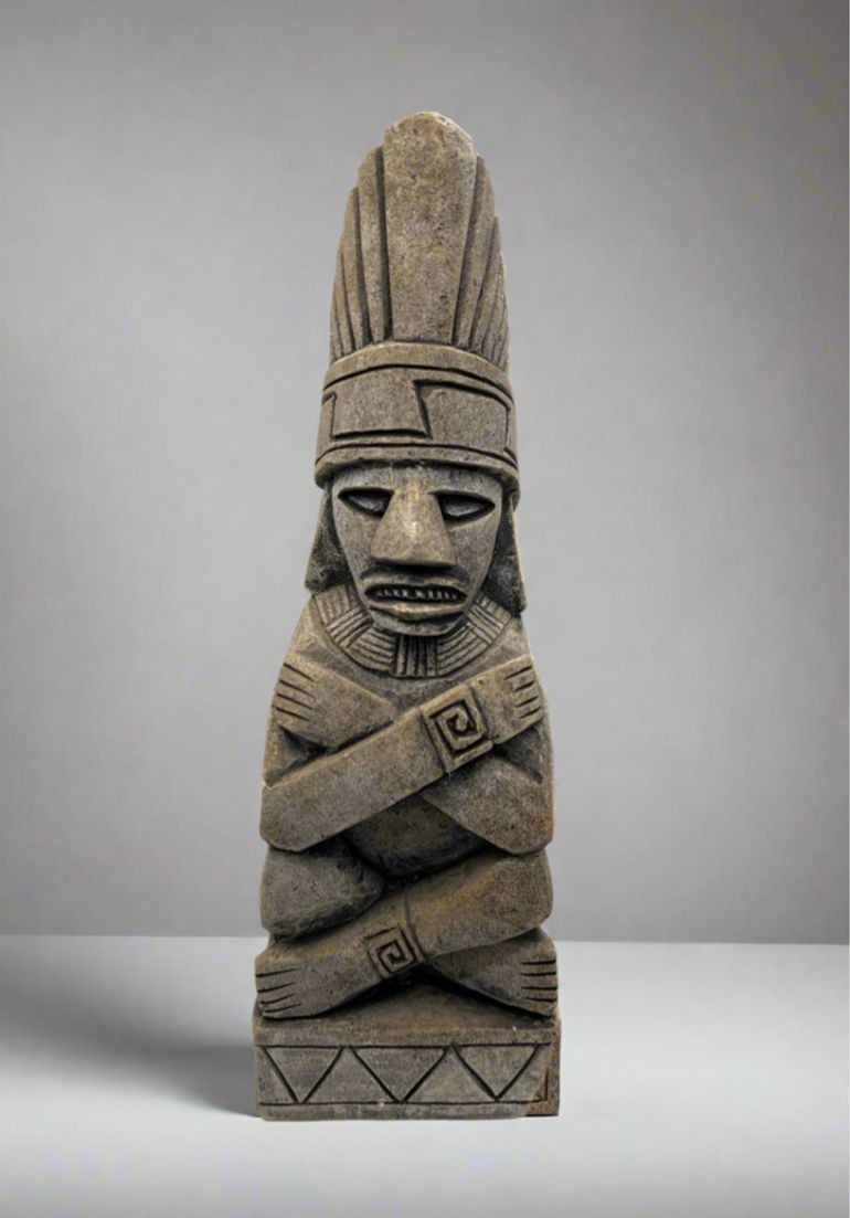 A carved gray stone bookend depicting a seated Aztec or Mesoamerican figure wearing a feathered headdress with incised geometric patterns on the base. - Photo 1