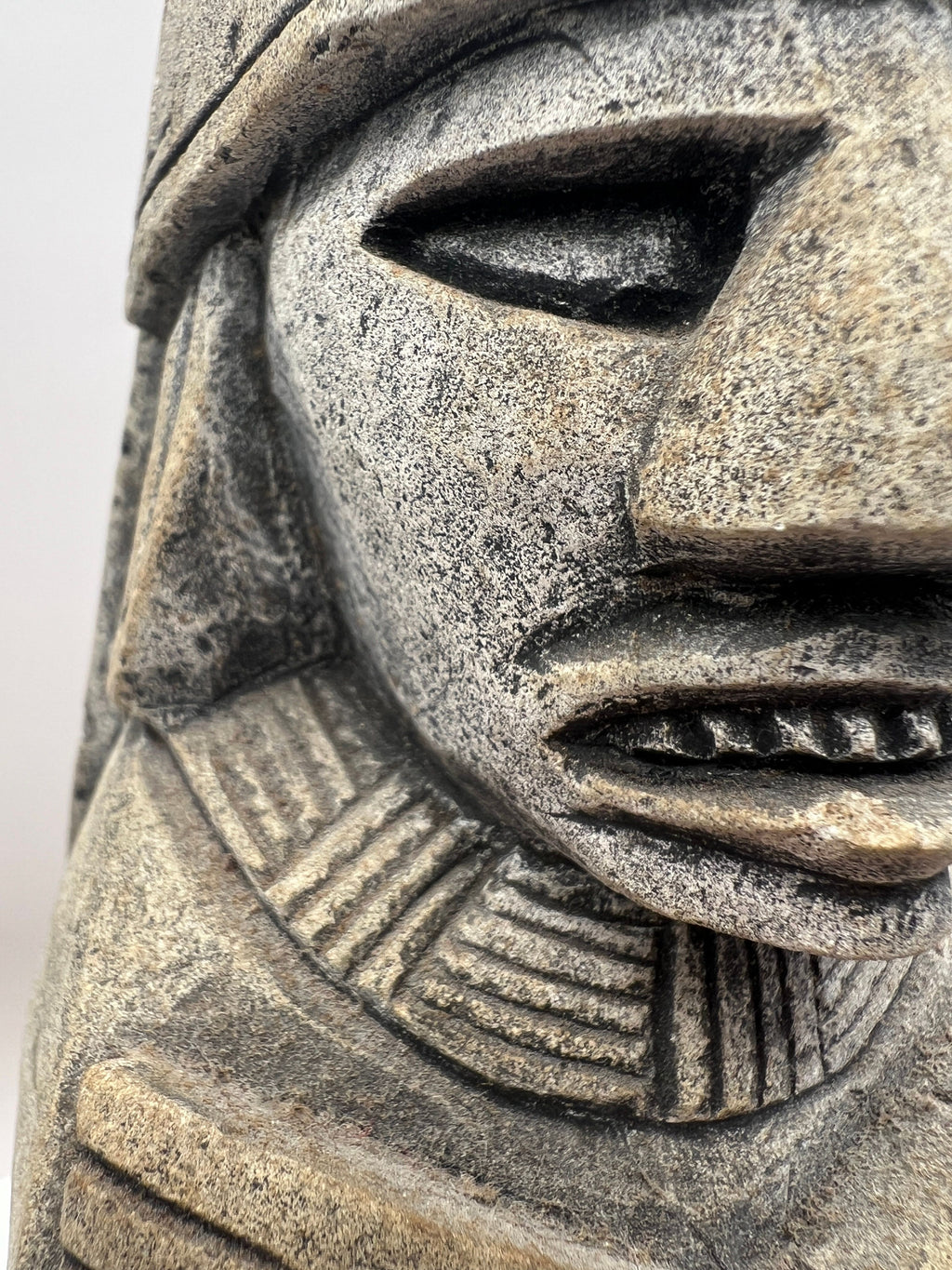 A carved gray stone bookend depicting a seated Aztec or Mesoamerican figure wearing a feathered headdress with incised geometric patterns on the base. - Photo 3