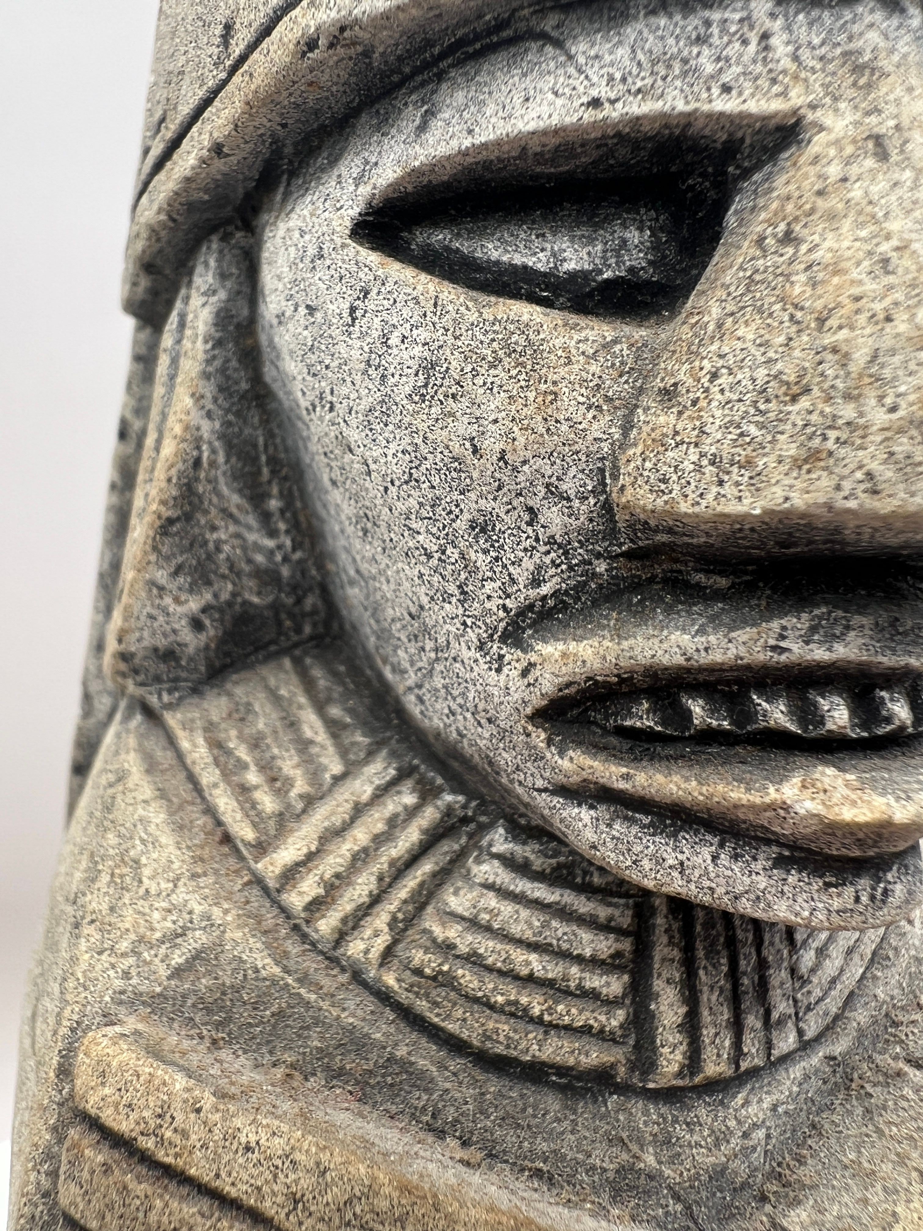 A carved gray stone bookend depicting a seated Aztec or Mesoamerican figure wearing a feathered headdress with incised geometric patterns on the base. - Photo 3