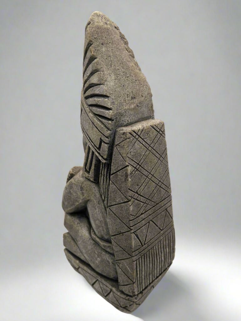 A carved gray stone bookend depicting a seated Aztec or Mesoamerican figure wearing a feathered headdress with incised geometric patterns on the base. - Photo 6