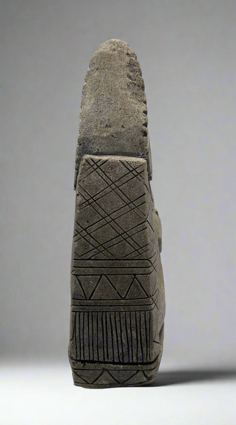 A carved gray stone bookend depicting a seated Aztec or Mesoamerican figure wearing a feathered headdress with incised geometric patterns on the base. - Photo 7