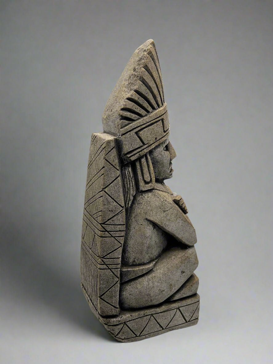 A carved gray stone bookend depicting a seated Aztec or Mesoamerican figure wearing a feathered headdress with incised geometric patterns on the base. - Photo 9