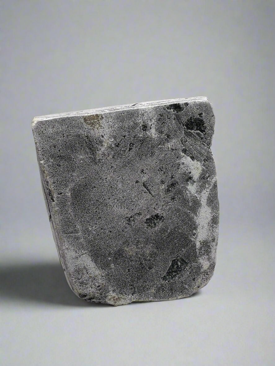 A carved gray stone bookend depicting a seated Aztec or Mesoamerican figure wearing a feathered headdress with incised geometric patterns on the base. - Photo 10