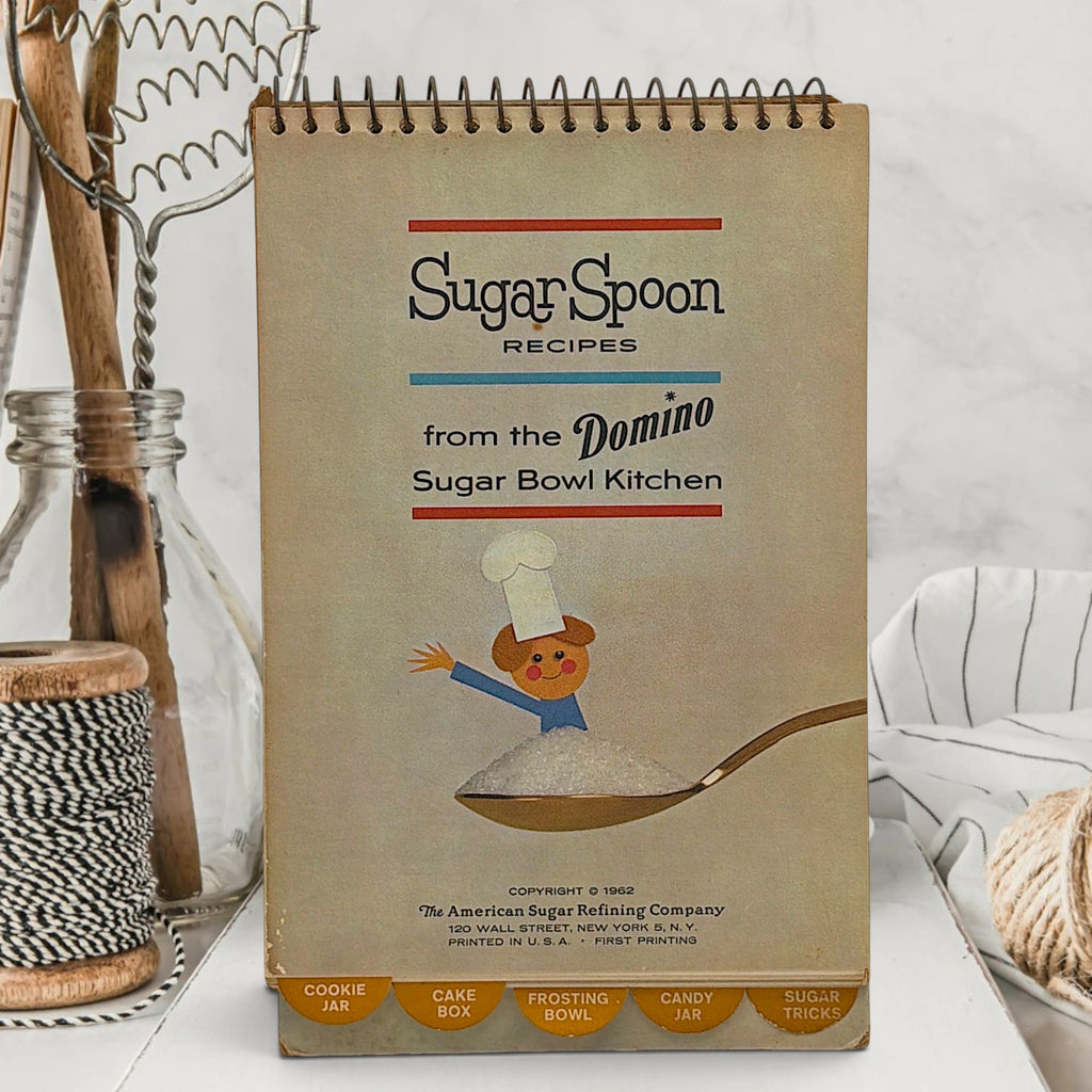A vintage spiral-bound recipe easel stand featuring an illustration of a tiny chef piloting an antique floral sugar bowl hot air balloon over sugar dunes under a blue sky. - Photo 2