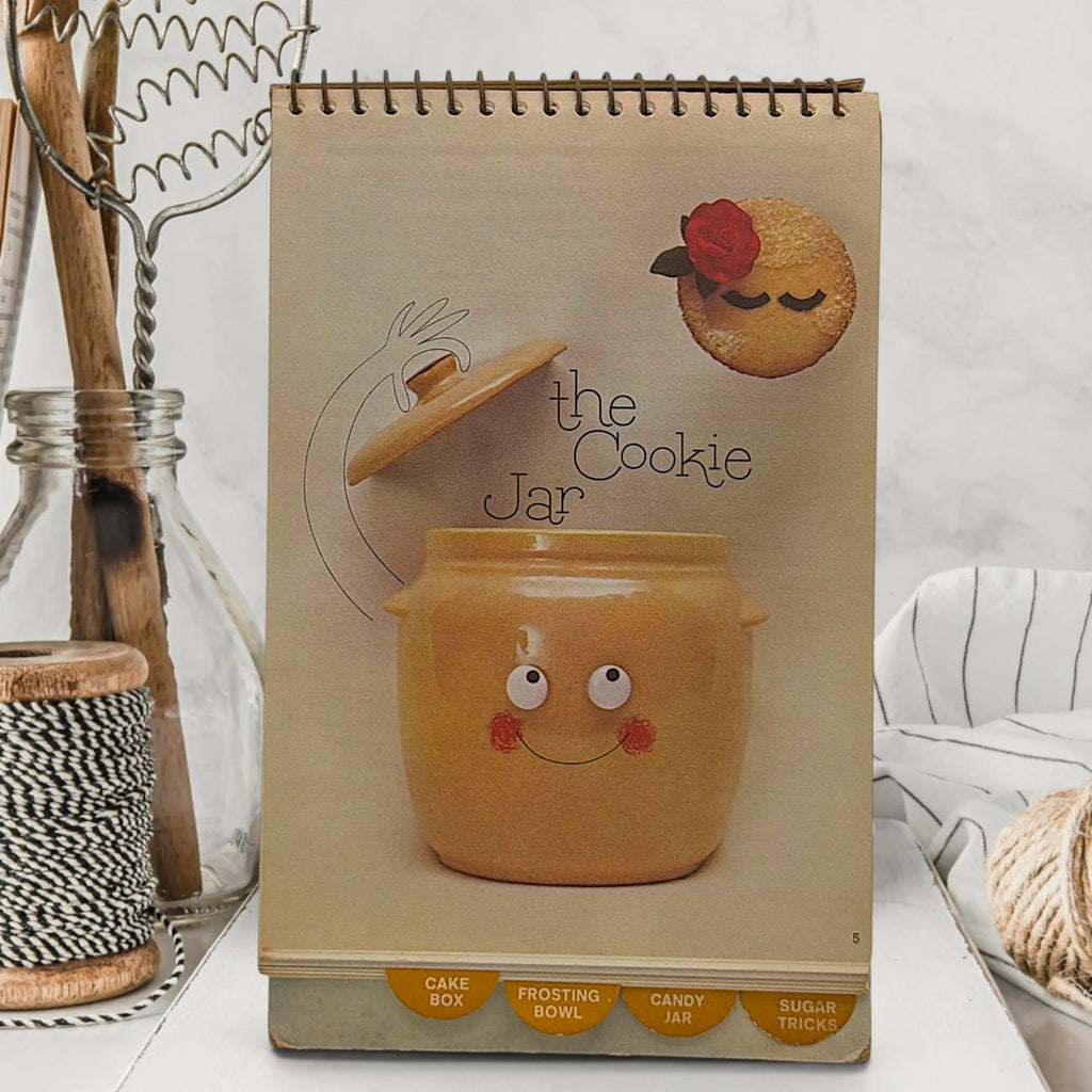 A vintage spiral-bound recipe easel stand featuring an illustration of a tiny chef piloting an antique floral sugar bowl hot air balloon over sugar dunes under a blue sky. - Photo 4