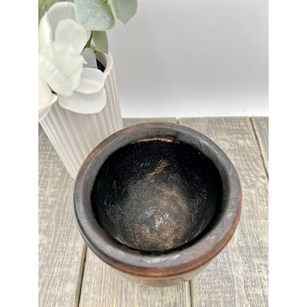 Antique dark wood mortar and pestle with worn interior on rustic wooden surface.