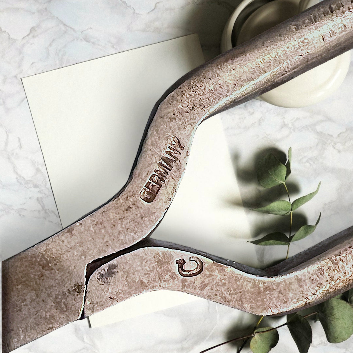 Two antique forged steel Marcel curling iron tongs with tapered points resting diagonally on white paper beside a dried eucalyptus branch. - Photo 2