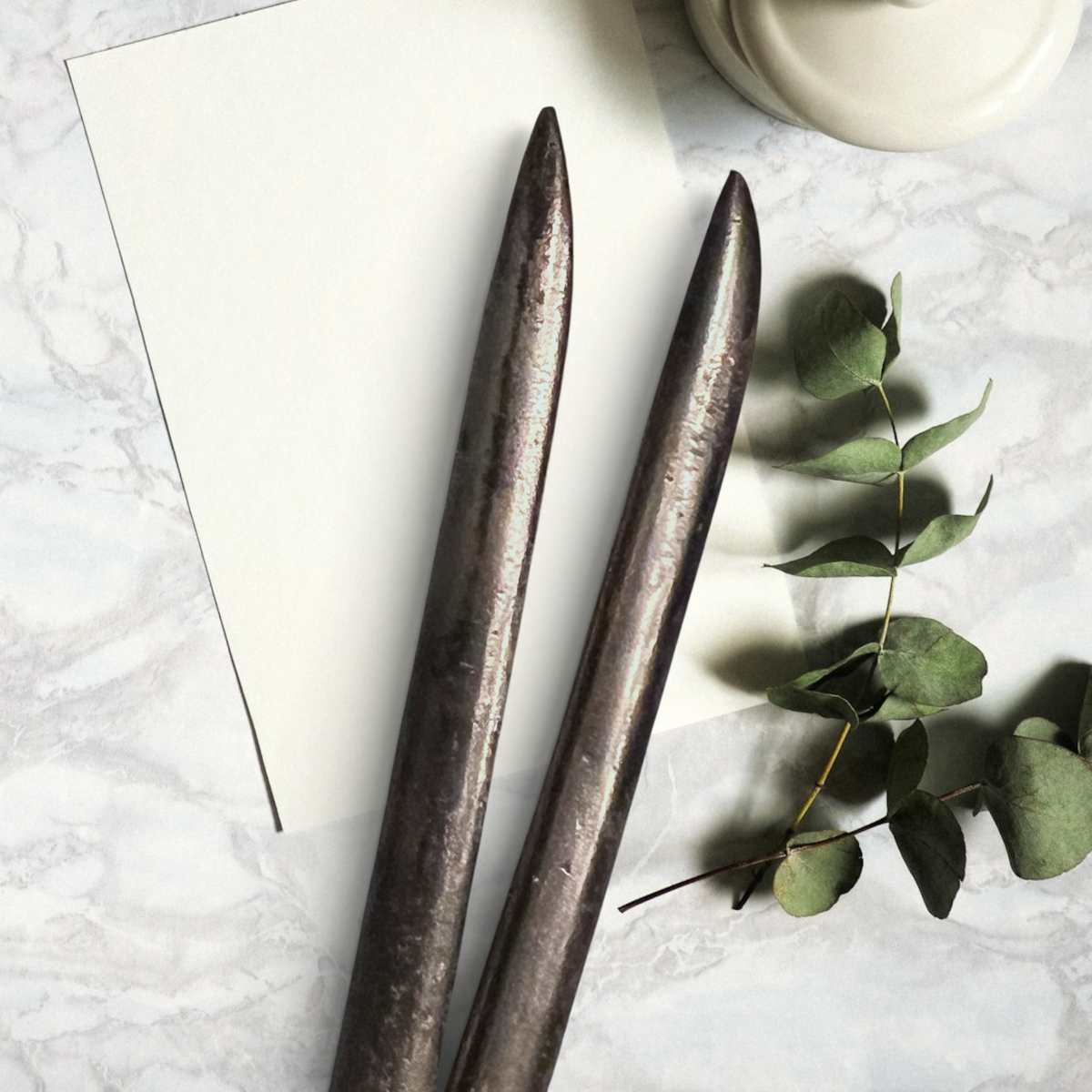 Two antique forged steel Marcel curling iron tongs with tapered points resting diagonally on white paper beside a dried eucalyptus branch. - Photo 3