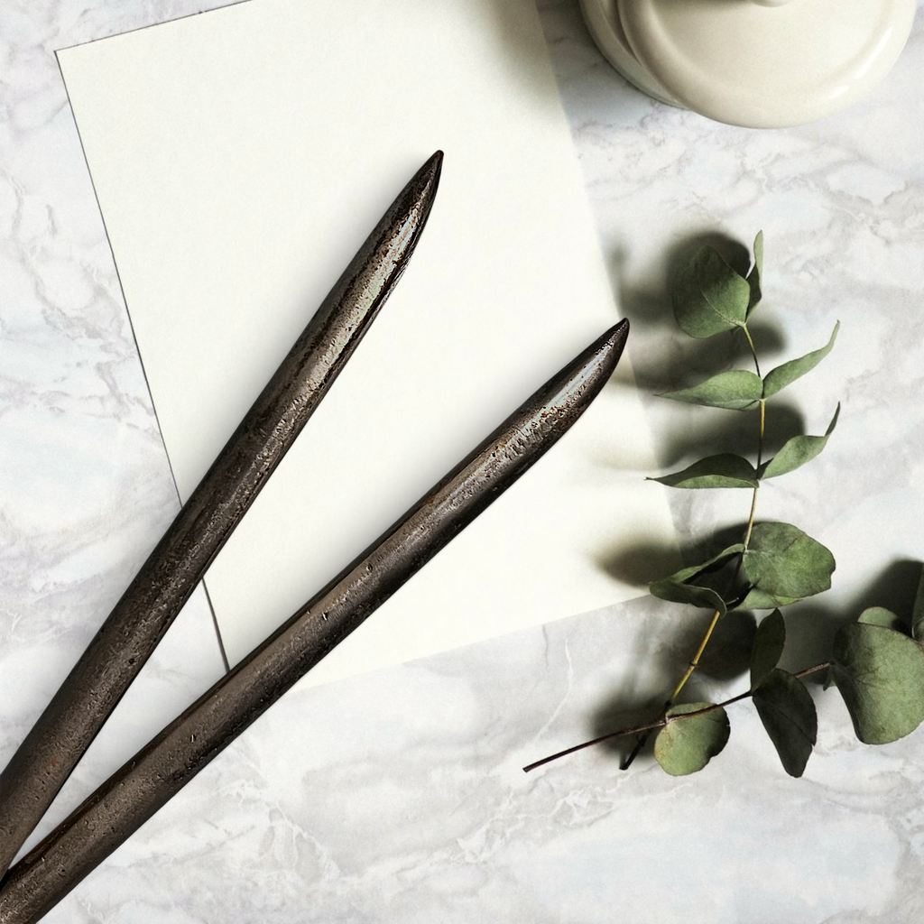 Two antique forged steel Marcel curling iron tongs with tapered points resting diagonally on white paper beside a dried eucalyptus branch. - Photo 8