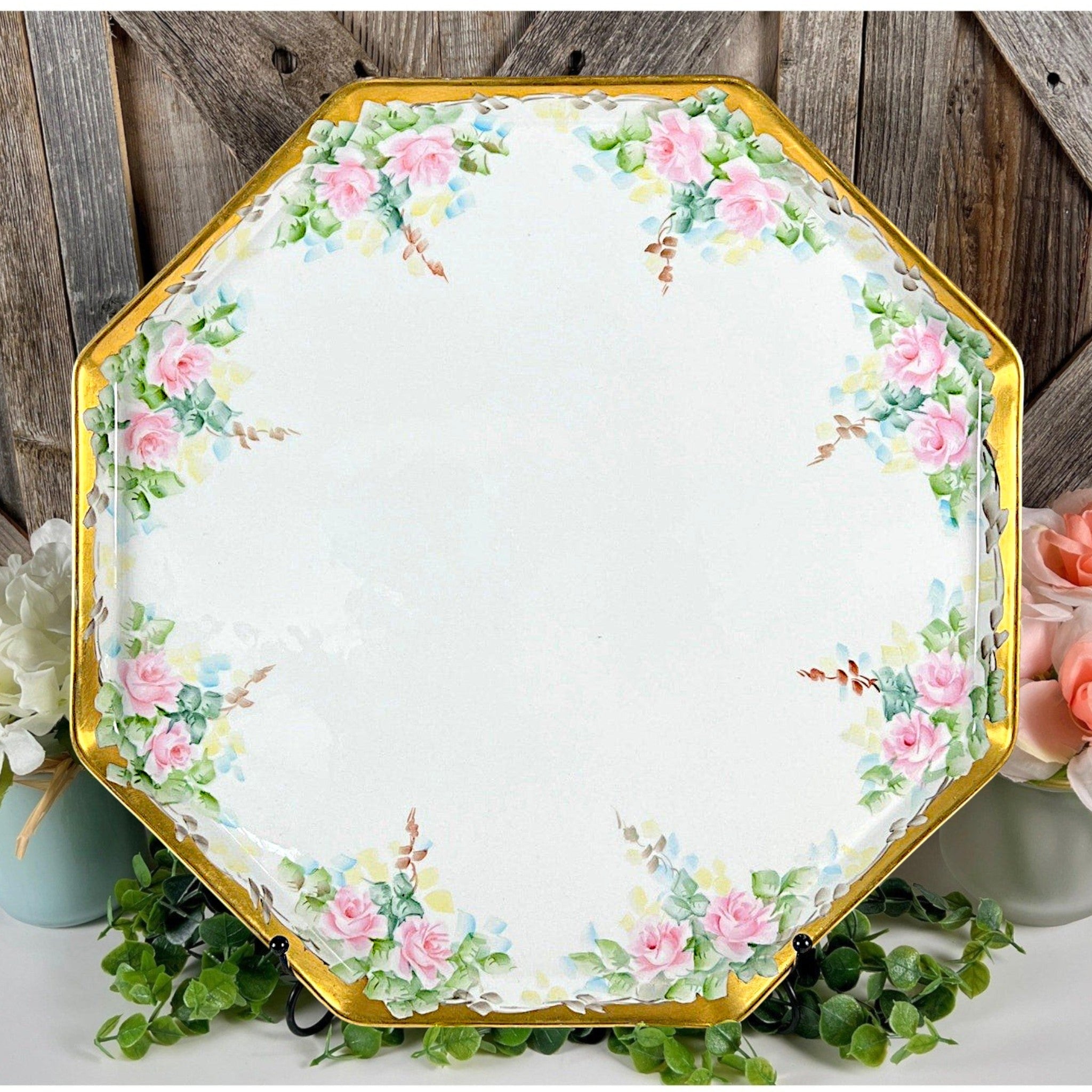 An antique white porcelain octagonal serving platter featuring a delicate gold-gilded rim, presented on a display stand among green foliage. - Photo 1