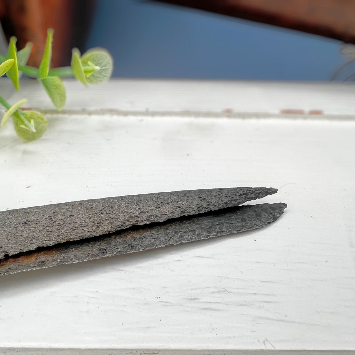 Antique hand-forged iron shears with rounded finger loops and tapered blades resting on a white surface beside a wooden textile bobbin. - Photo 2