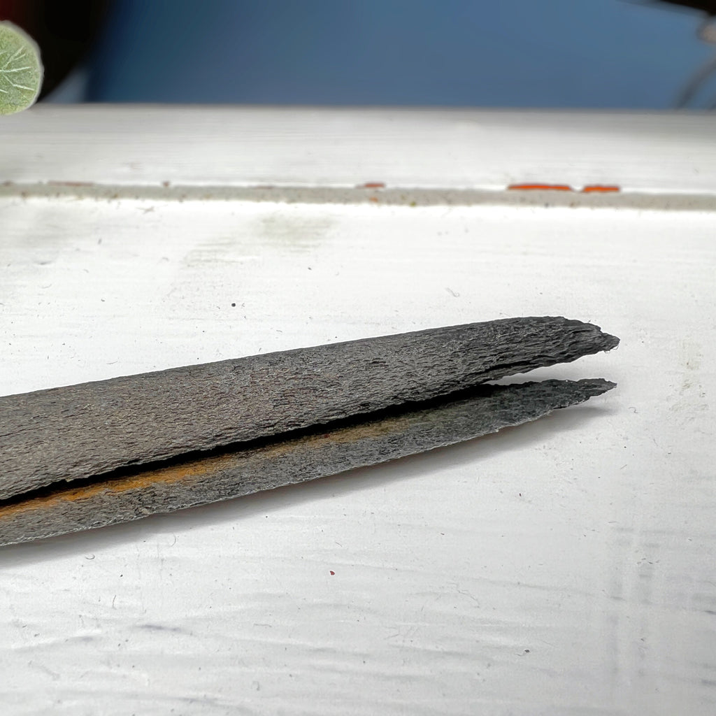Antique hand-forged iron shears with rounded finger loops and tapered blades resting on a white surface beside a wooden textile bobbin. - Photo 3