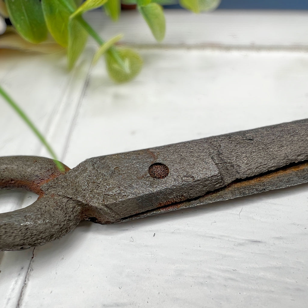 Antique hand-forged iron shears with rounded finger loops and tapered blades resting on a white surface beside a wooden textile bobbin. - Photo 4