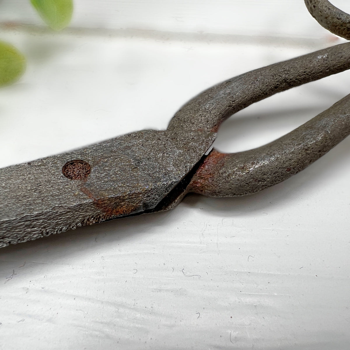 Antique hand-forged iron shears with rounded finger loops and tapered blades resting on a white surface beside a wooden textile bobbin. - Photo 5