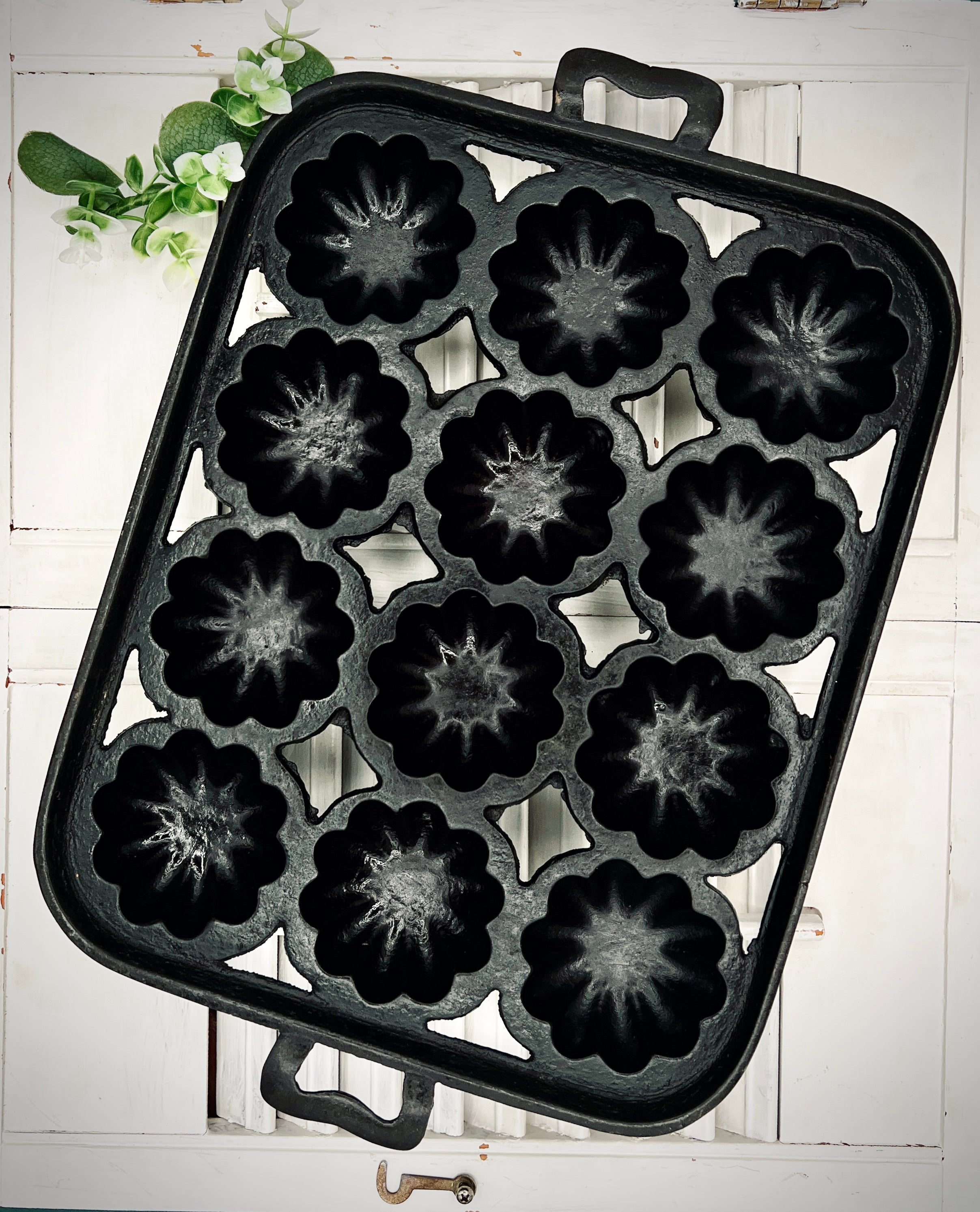 A black antique cast iron 12-cup gem pan with deeply fluted scalloped molds in a 4-4-4 open-frame layout and wavy stylized handles at both ends. - Photo 1