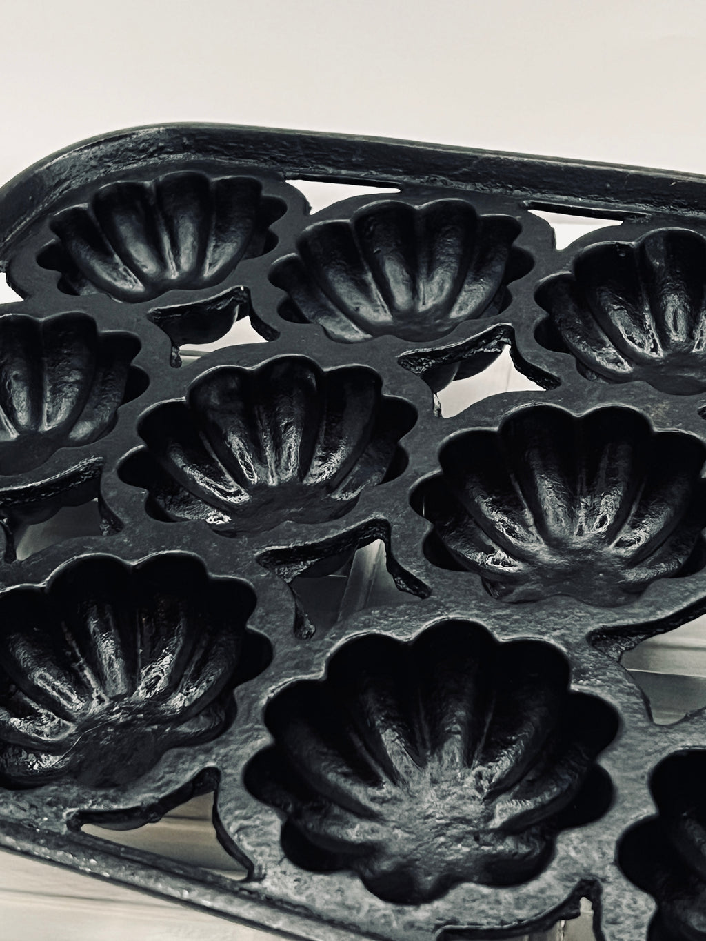 A black antique cast iron 12-cup gem pan with deeply fluted scalloped molds in a 4-4-4 open-frame layout and wavy stylized handles at both ends. - Photo 2