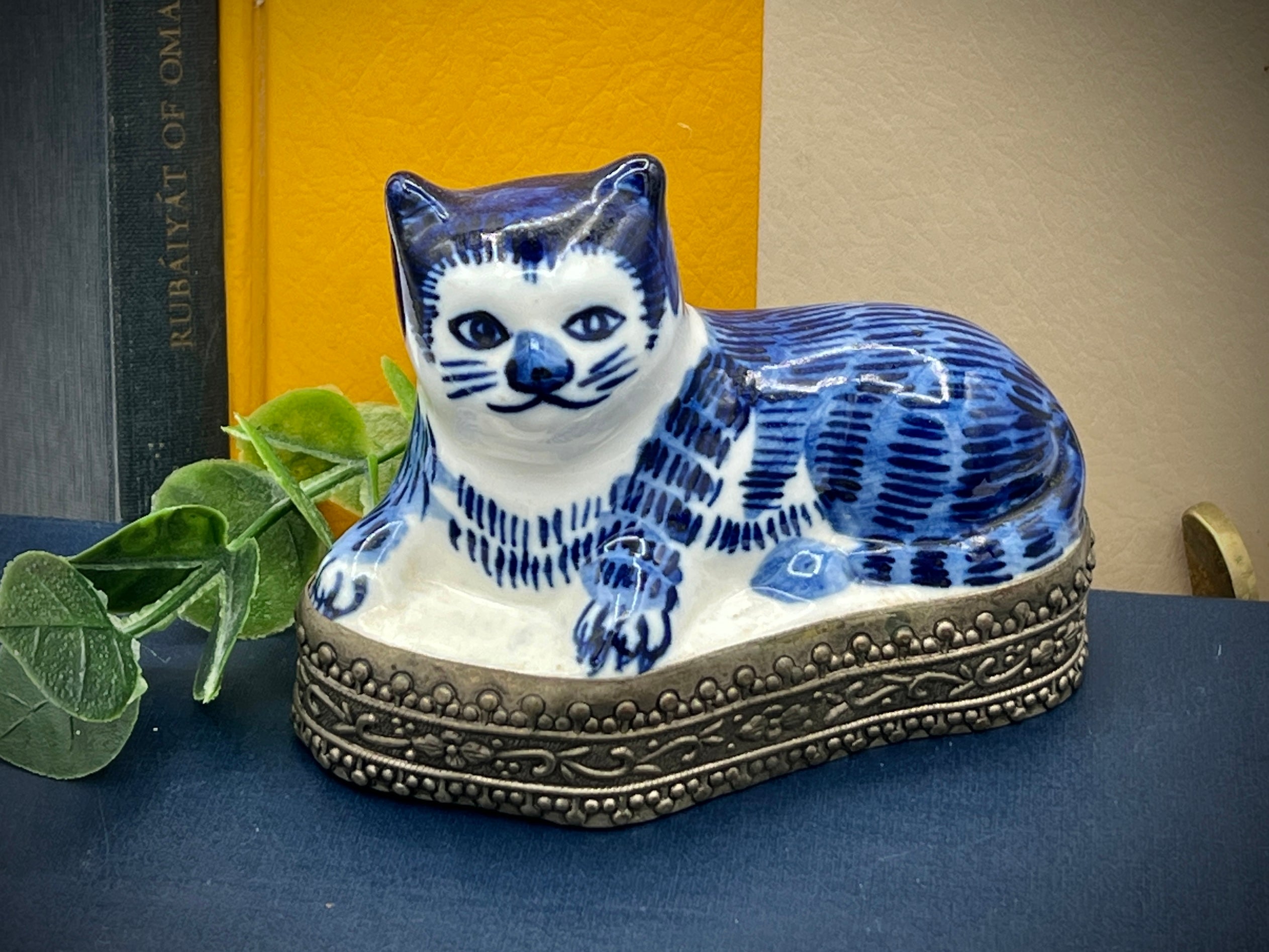 A vintage blue and white glazed porcelain cat figurine with cobalt blue painted patterns resting on an ornate embossed metal gallery base. - Photo 1