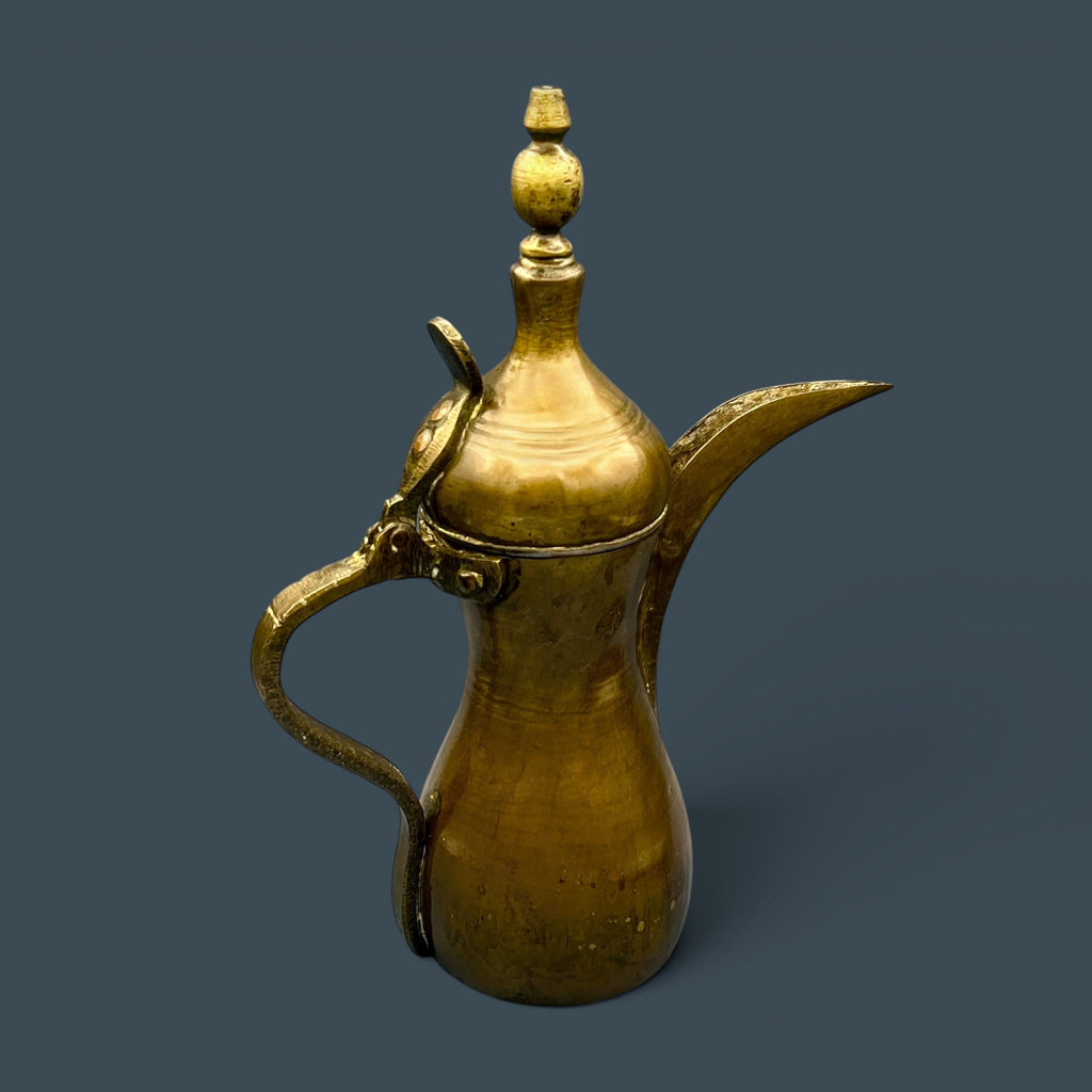 An antique hand-forged brass pitcher with a tapered neck and warm golden-brown patina, displayed against a dark background. - Photo 1