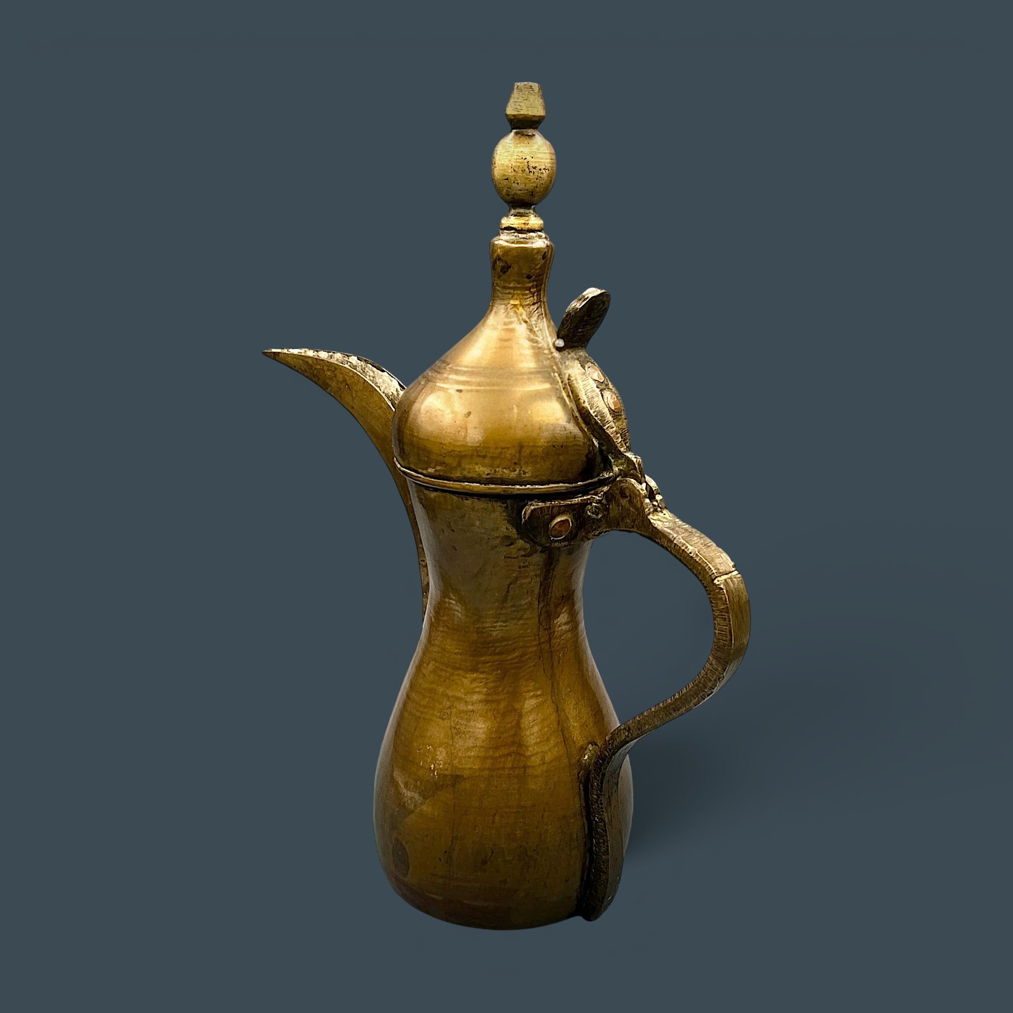 An antique hand-forged brass pitcher with a tapered neck and warm golden-brown patina, displayed against a dark background. - Photo 3