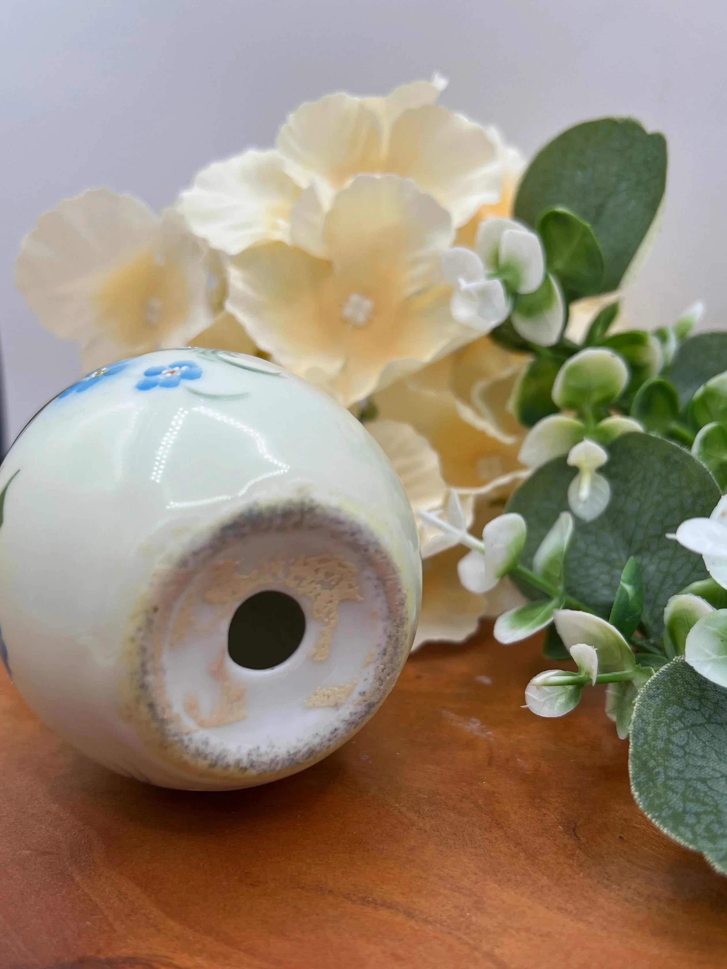 White ceramic egg shaker with a central hole on a wooden surface with flowers in the background