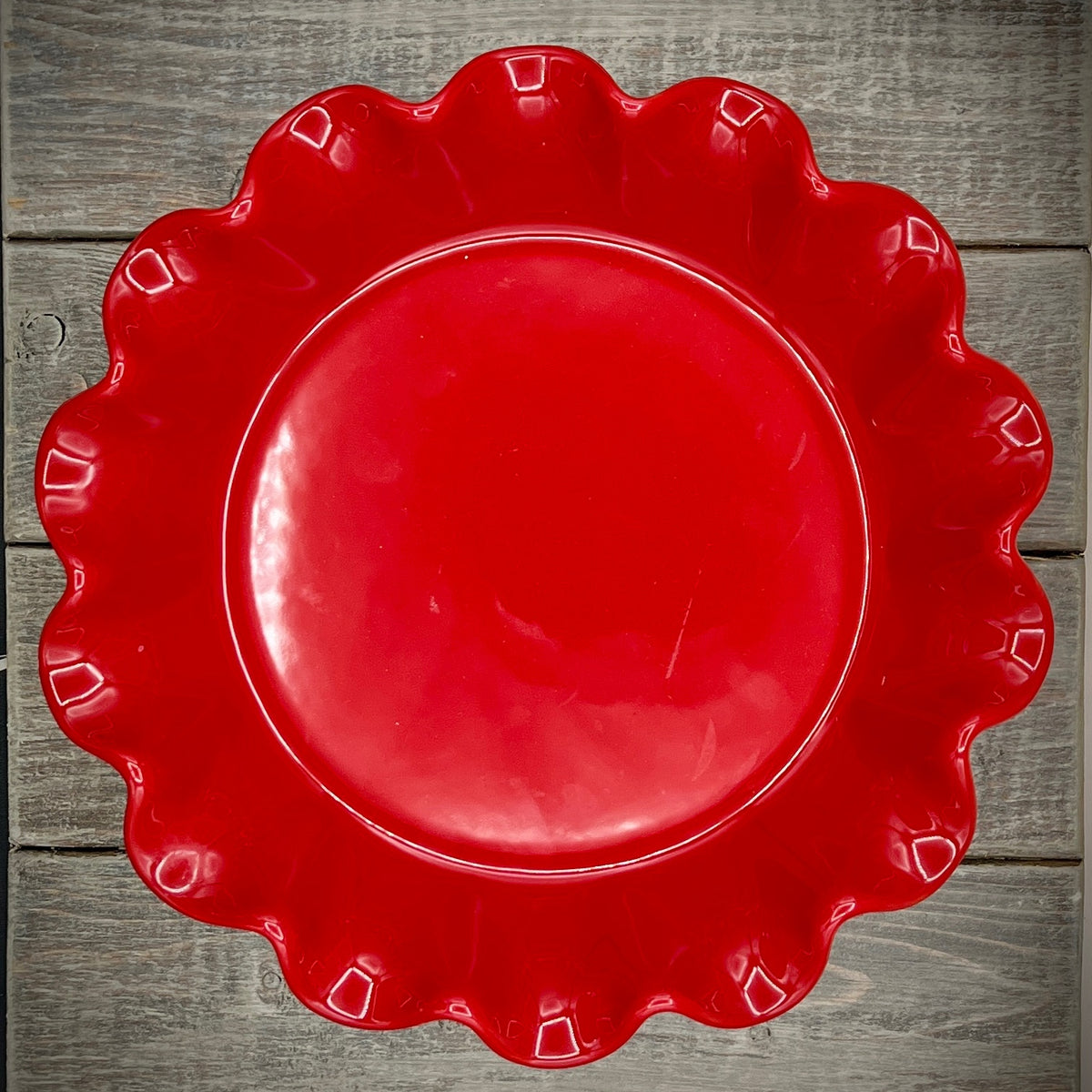 Emile Henry red ceramic deep ruffled pie dish displayed upright on a wooden surface showing its scalloped rim and glossy crimson glaze. - Photo 2