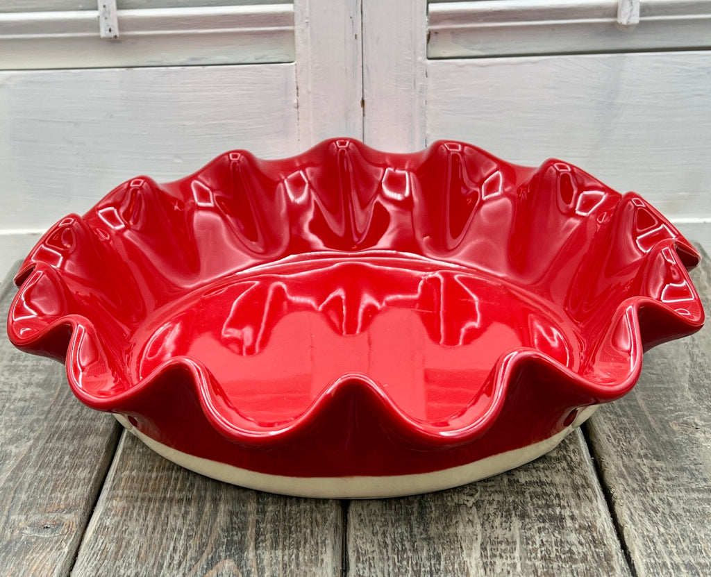 Emile Henry red ceramic deep ruffled pie dish displayed upright on a wooden surface showing its scalloped rim and glossy crimson glaze. - Photo 3