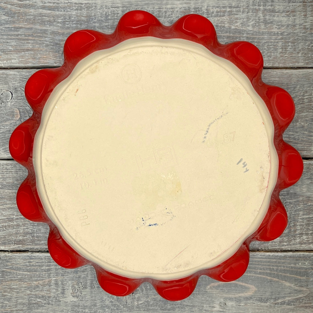 Emile Henry red ceramic deep ruffled pie dish displayed upright on a wooden surface showing its scalloped rim and glossy crimson glaze. - Photo 4
