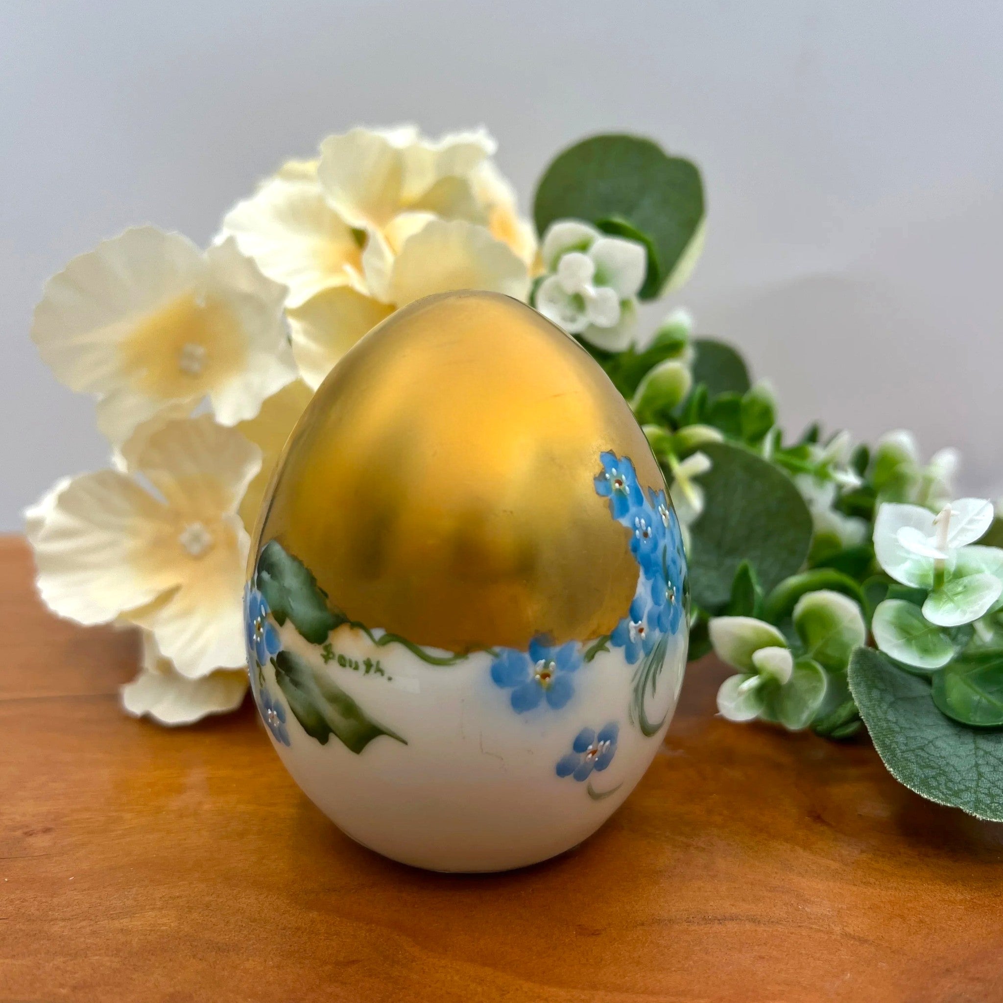 An antique porcelain egg-shaped shaker featuring hand-painted blue forget-me-not flowers along the base and heavy, lustrous gold gilding across the top, set against a background of cream flowers and green foliage. - Photo 2