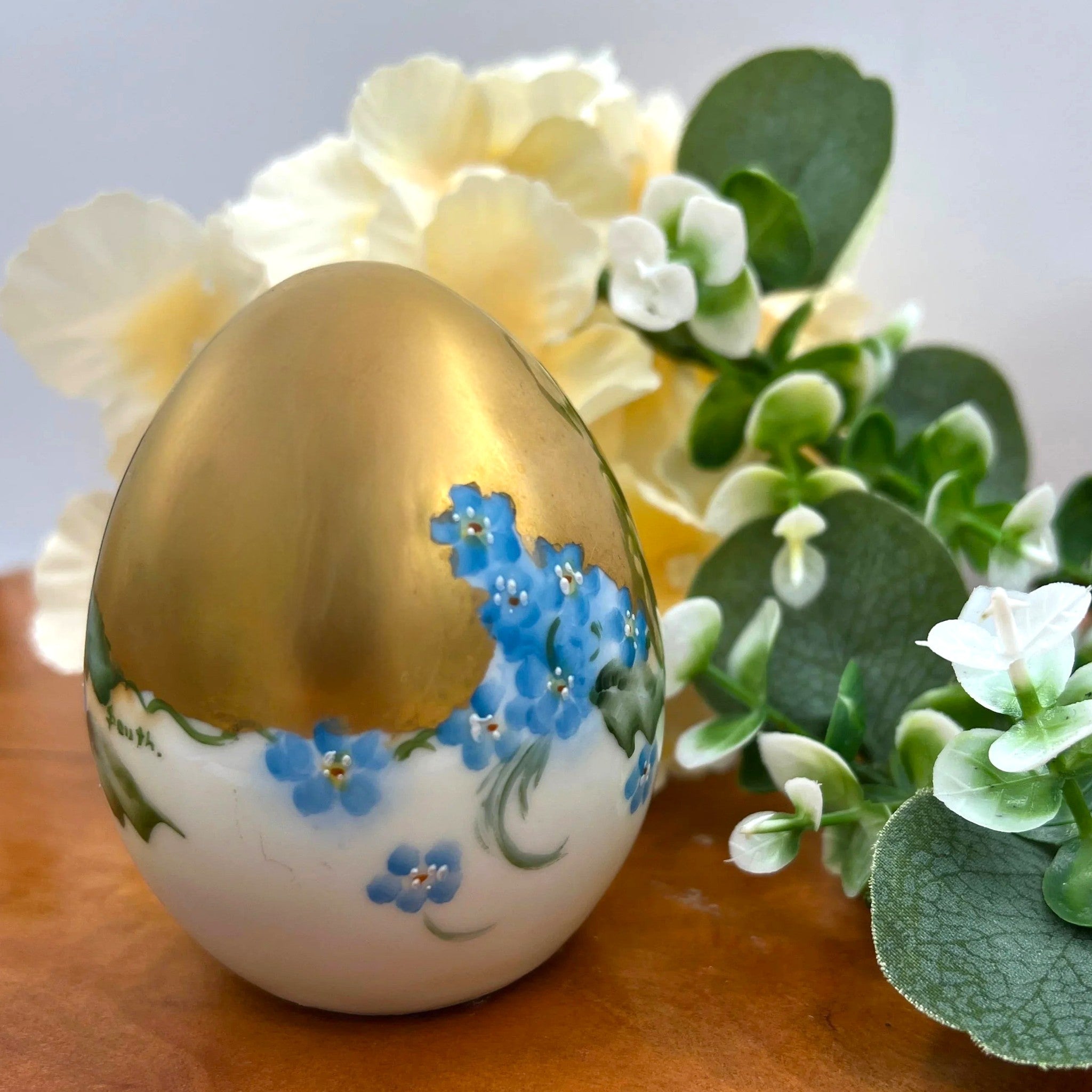 An antique porcelain egg-shaped shaker featuring hand-painted blue forget-me-not flowers along the base and heavy, lustrous gold gilding across the top, set against a background of cream flowers and green foliage. - Photo 3
