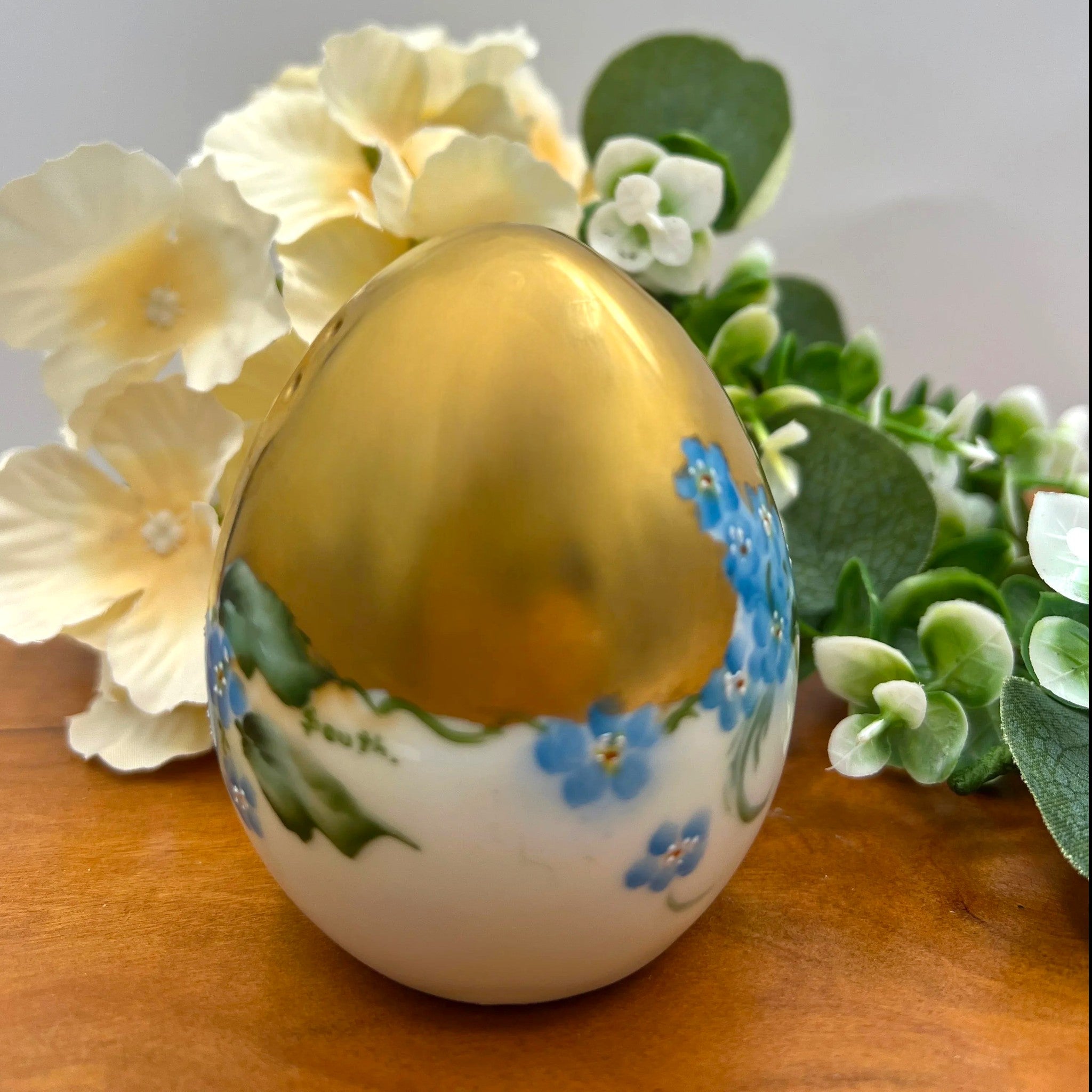 An antique porcelain egg-shaped shaker featuring hand-painted blue forget-me-not flowers along the base and heavy, lustrous gold gilding across the top, set against a background of cream flowers and green foliage. - Photo 4