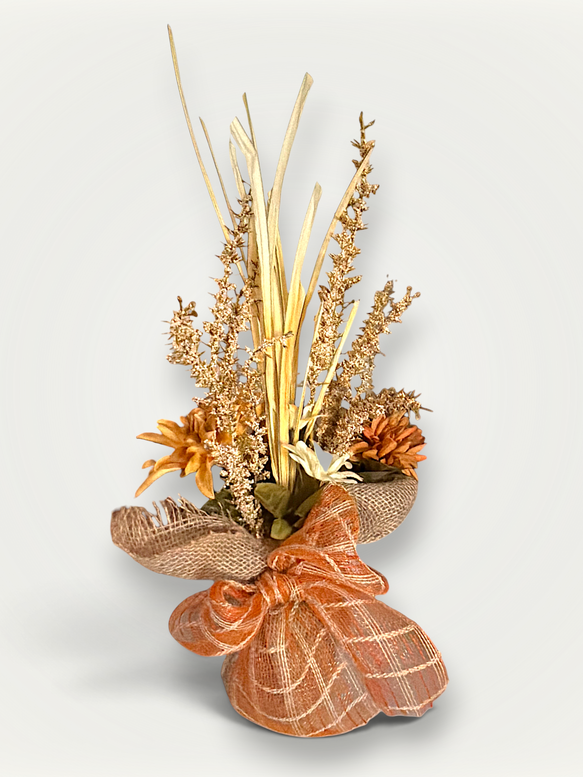 Handcrafted fall floral arrangement featuring an orange mesh bow, burlap wrapped base, faux flowers, and vertical dried botanical stalks.