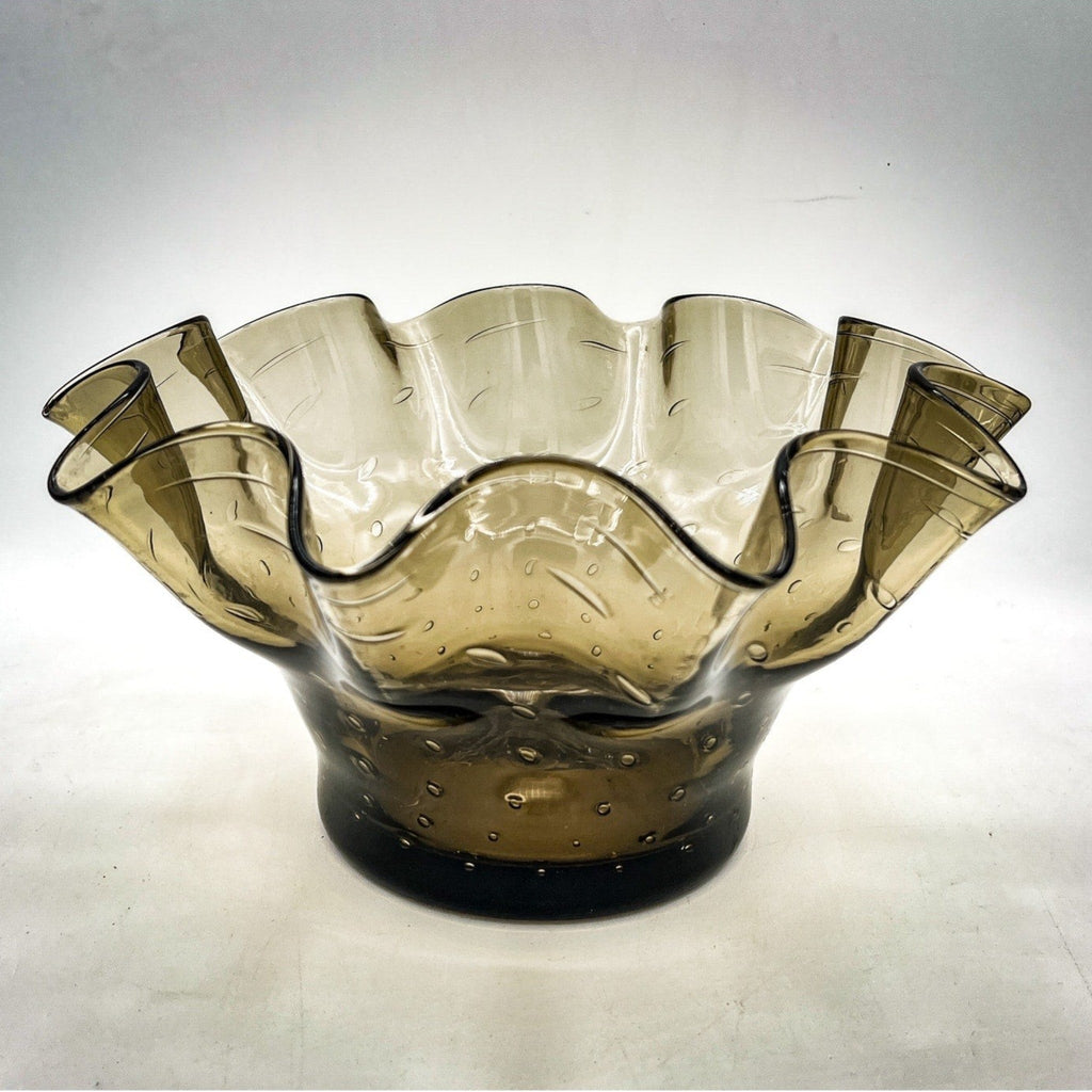 A smoky gray hand-blown art glass console bowl with a thick base featuring a neat row of controlled bubbles and a wide, undulating crimped ruffled rim flared outward against a white background. - Photo 1