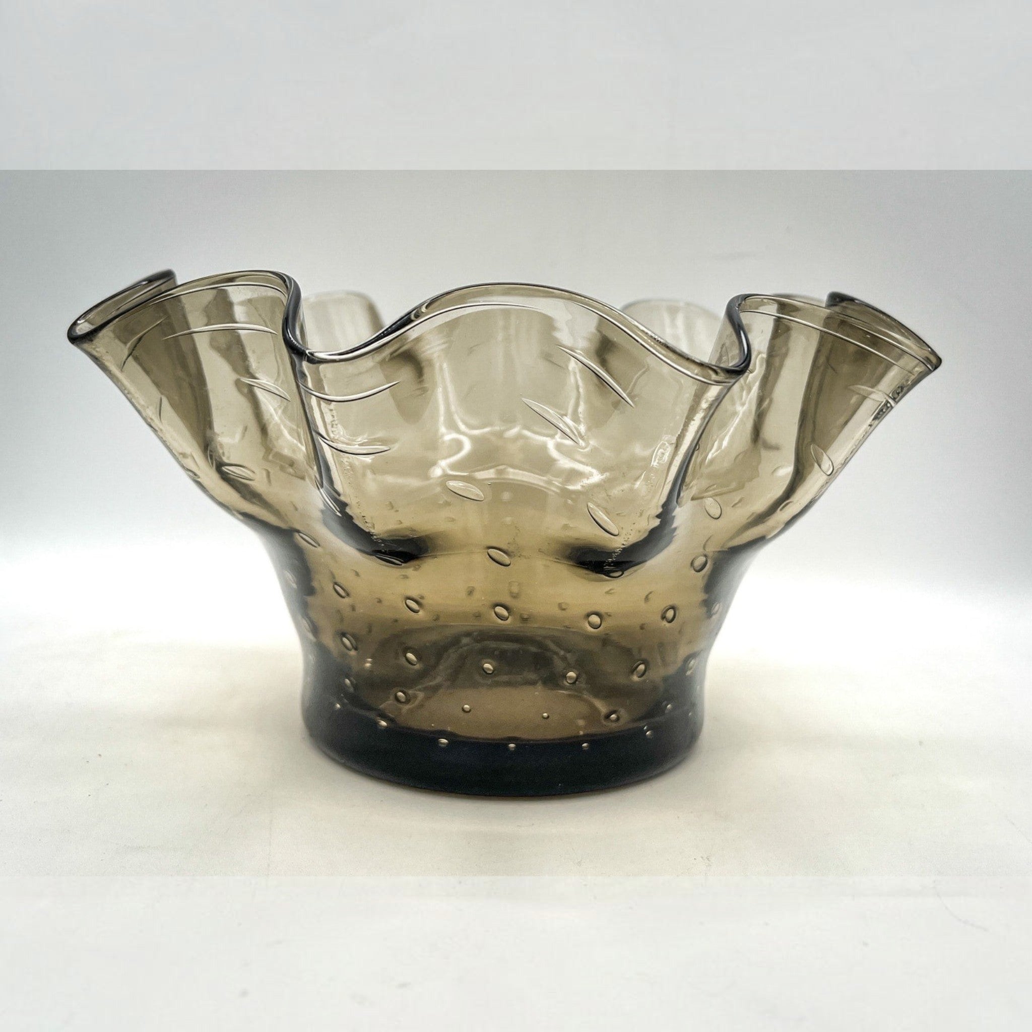 A smoky gray hand-blown art glass console bowl with a thick base featuring a neat row of controlled bubbles and a wide, undulating crimped ruffled rim flared outward against a white background. - Photo 2