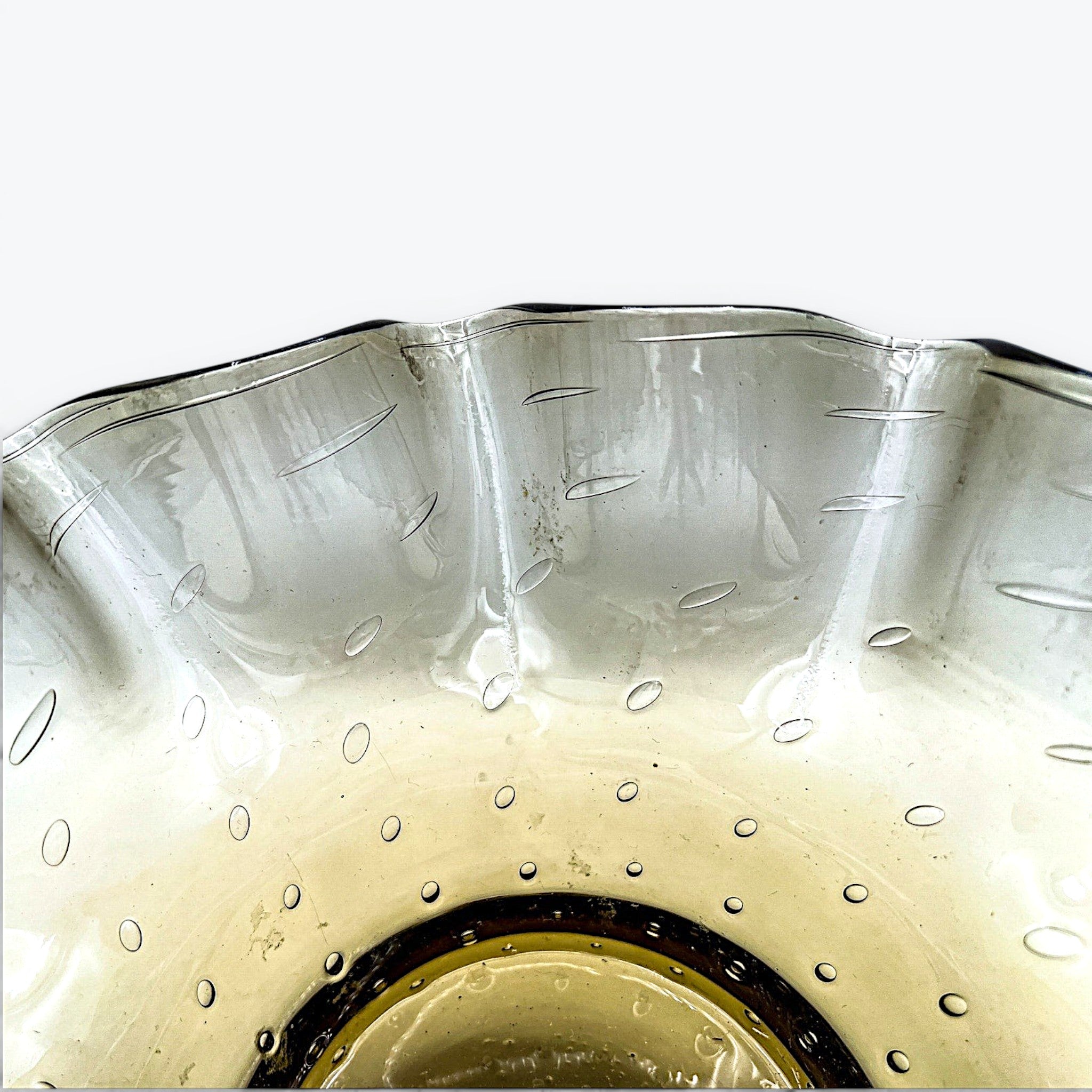 A smoky gray hand-blown art glass console bowl with a thick base featuring a neat row of controlled bubbles and a wide, undulating crimped ruffled rim flared outward against a white background. - Photo 3