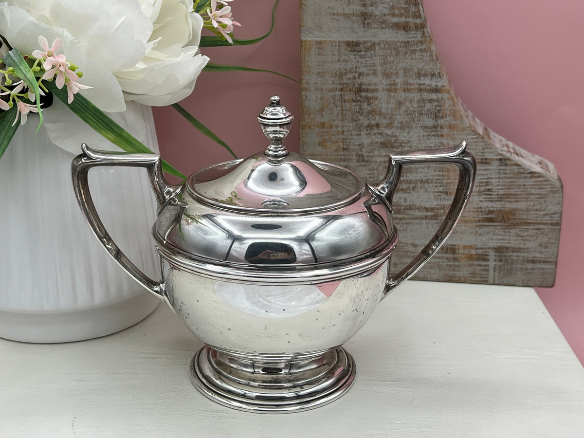 Antique William B. Durgin sterling silver two-handled covered sugar bowl with a polished urn-shaped body, stepped pedestal base, and matching domed lid topped with an urn finial displayed on a white tabletop. - Photo 11