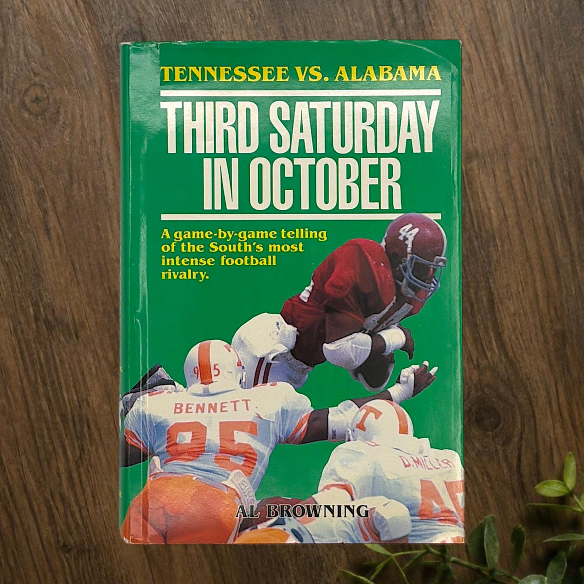 Hardcover book titled Third Saturday in October featuring a green dust jacket with bold white lettering and a full-color action illustration of Alabama and Tennessee football players in mid-tackle. - Photo 1