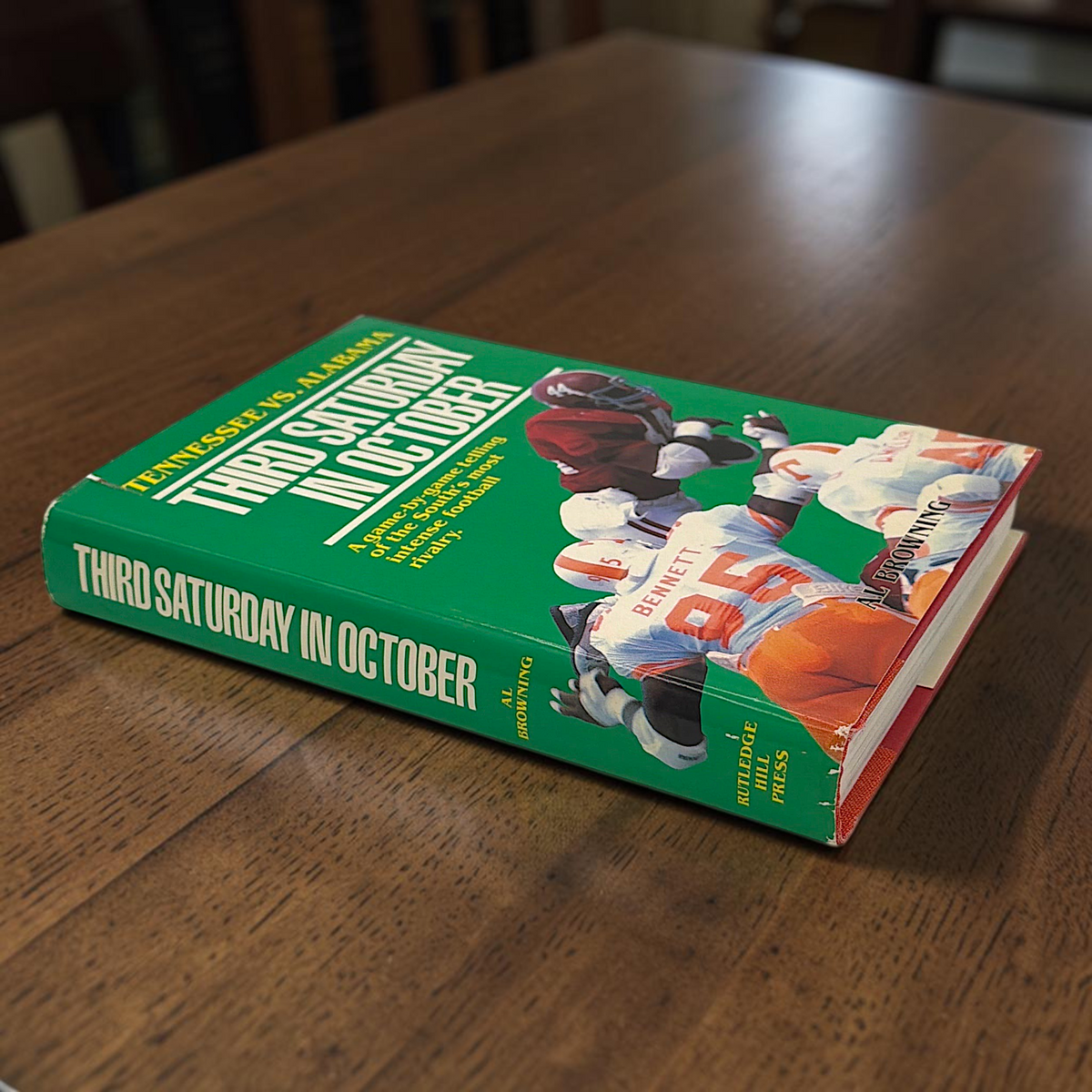 Hardcover book titled Third Saturday in October featuring a green dust jacket with bold white lettering and a full-color action illustration of Alabama and Tennessee football players in mid-tackle. - Photo 2