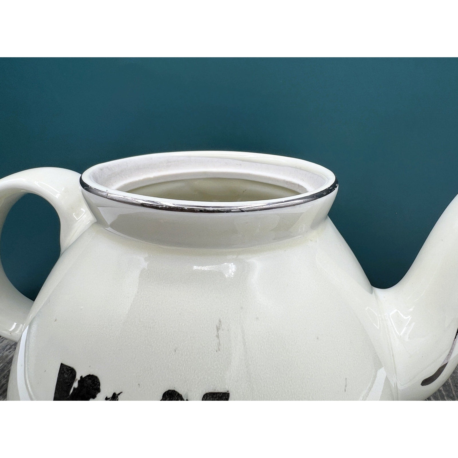 A warm cream ceramic teapot with a black silhouette tavern scene decal, showcasing a classic Art Deco streamlined design and platinum luster accents on the sweeping handle and spout. - Photo 4