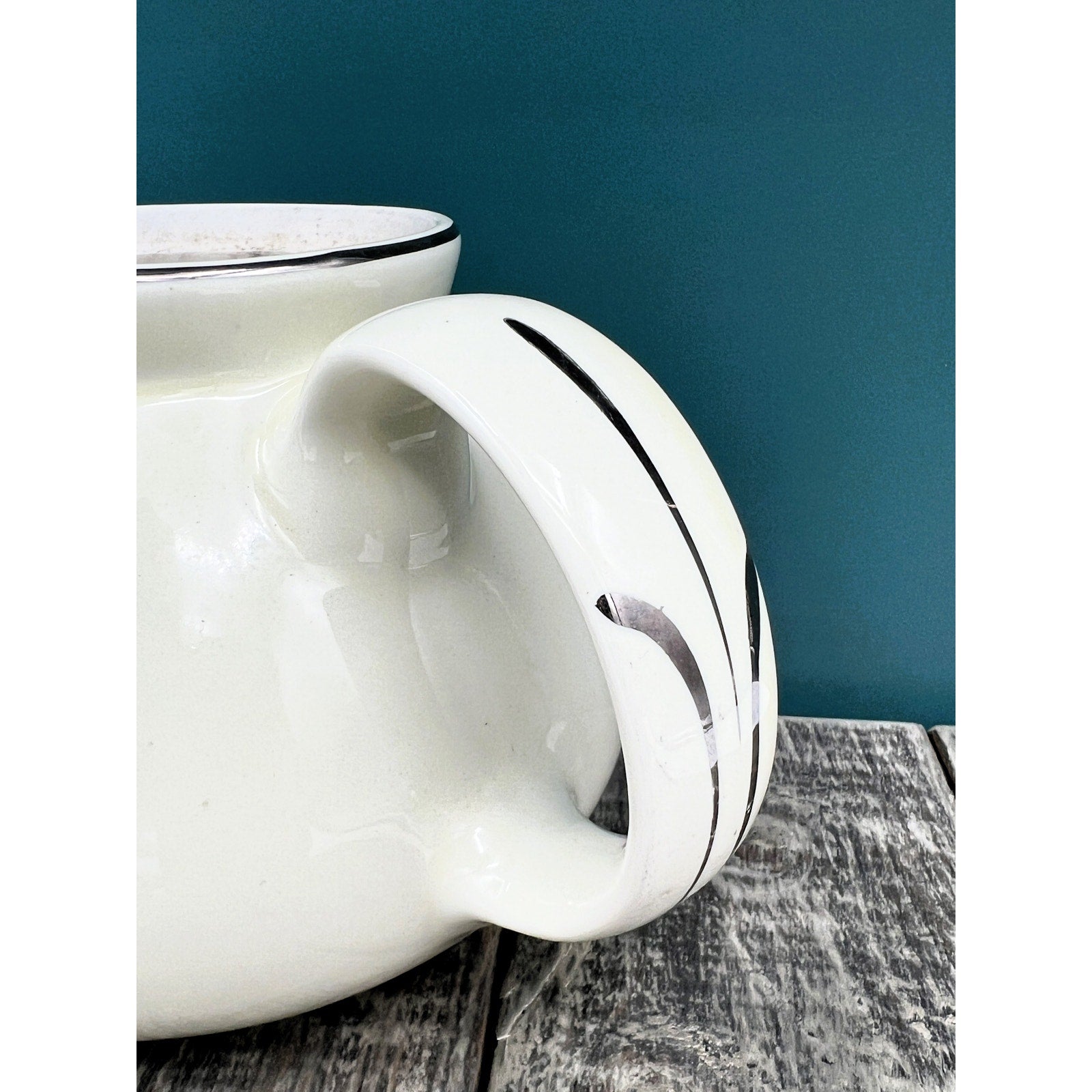A warm cream ceramic teapot with a black silhouette tavern scene decal, showcasing a classic Art Deco streamlined design and platinum luster accents on the sweeping handle and spout. - Photo 5
