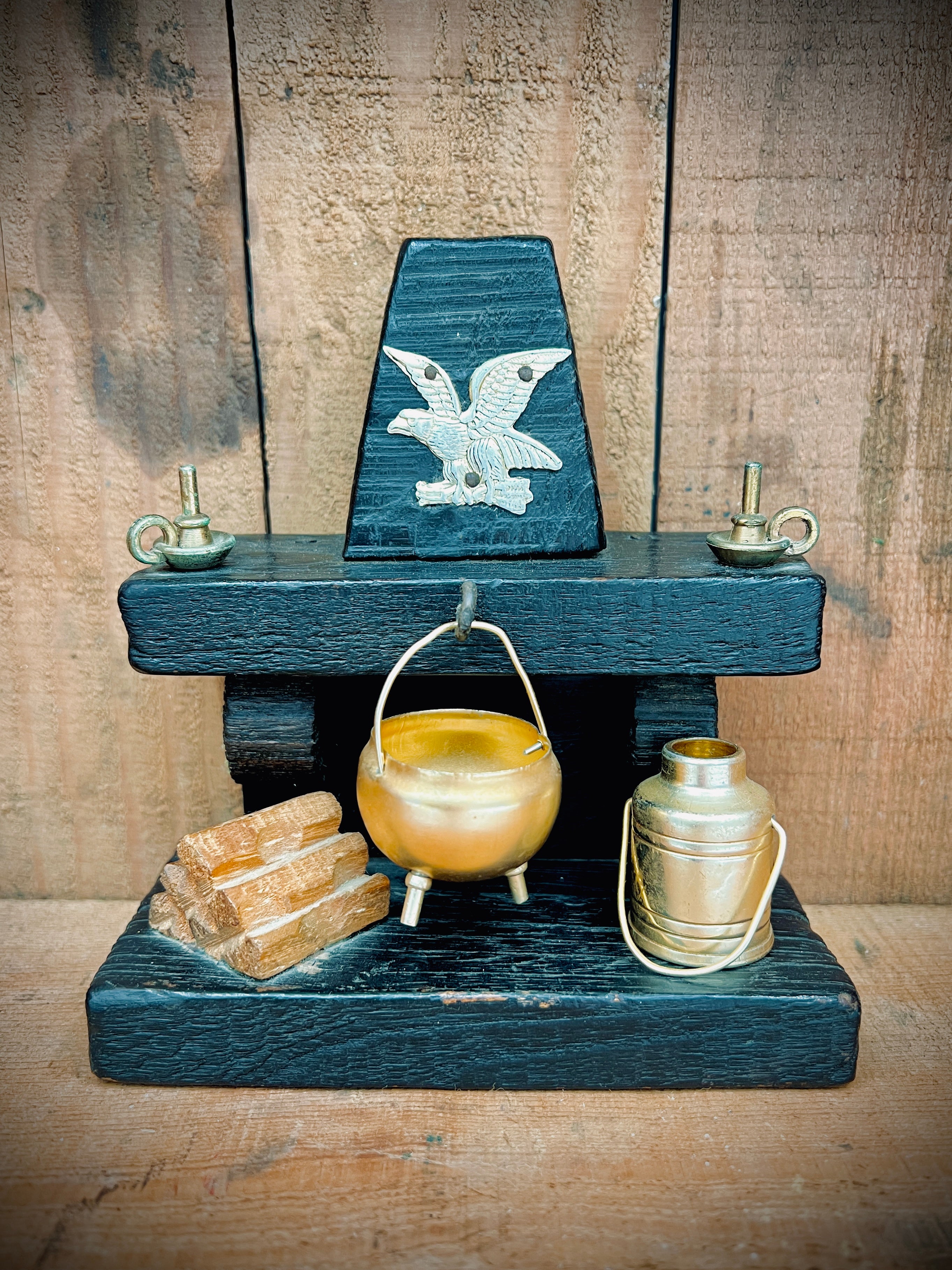 A vintage miniature fireplace hearth crafted from dark wood, showcasing tiny split logs and a gold-colored brass cauldron pot with a thin metal handle. - Photo 1