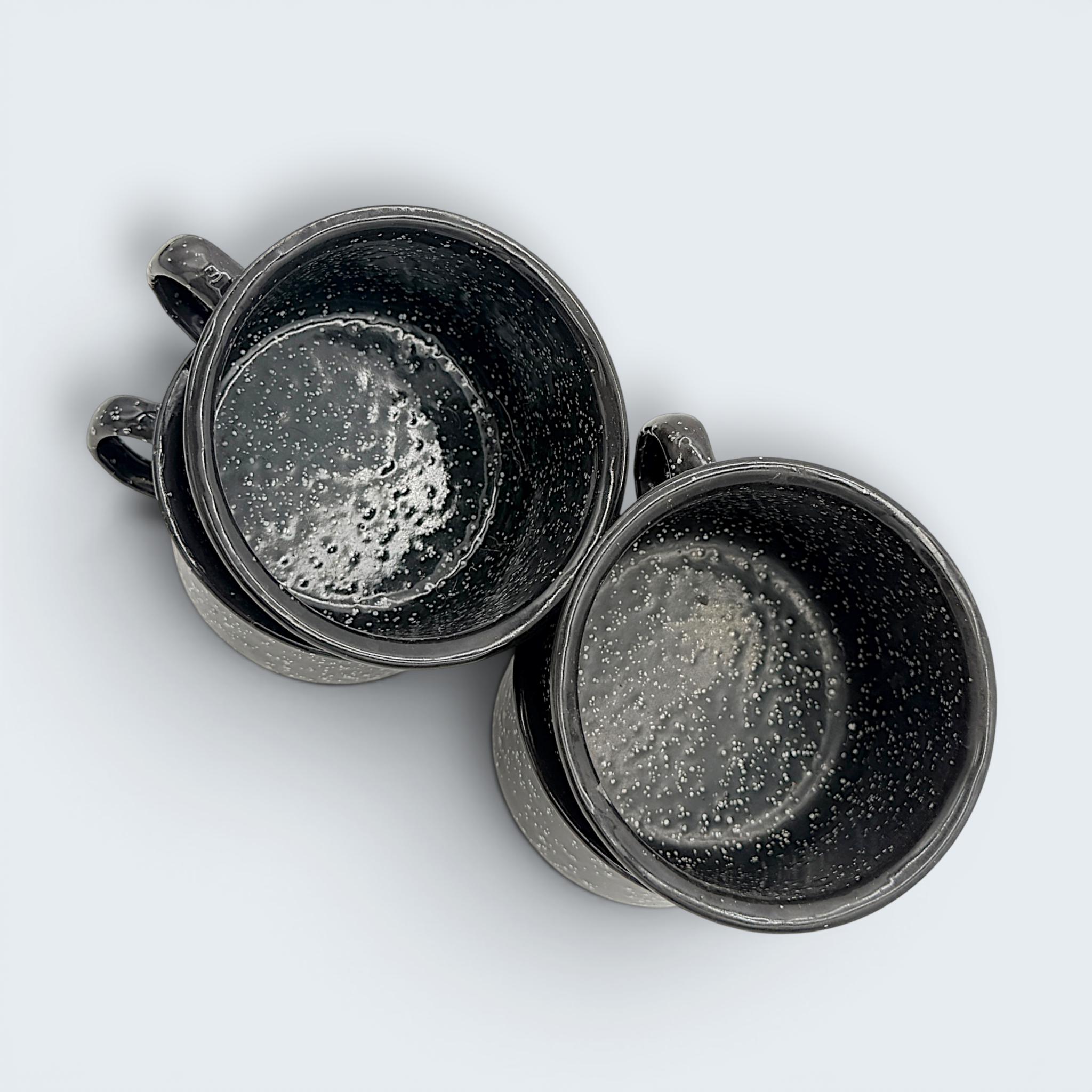 A vintage black enamel cup with white speckles and a single handle, showing a rustic interior with character-building wear at the bottom. - Photo 2
