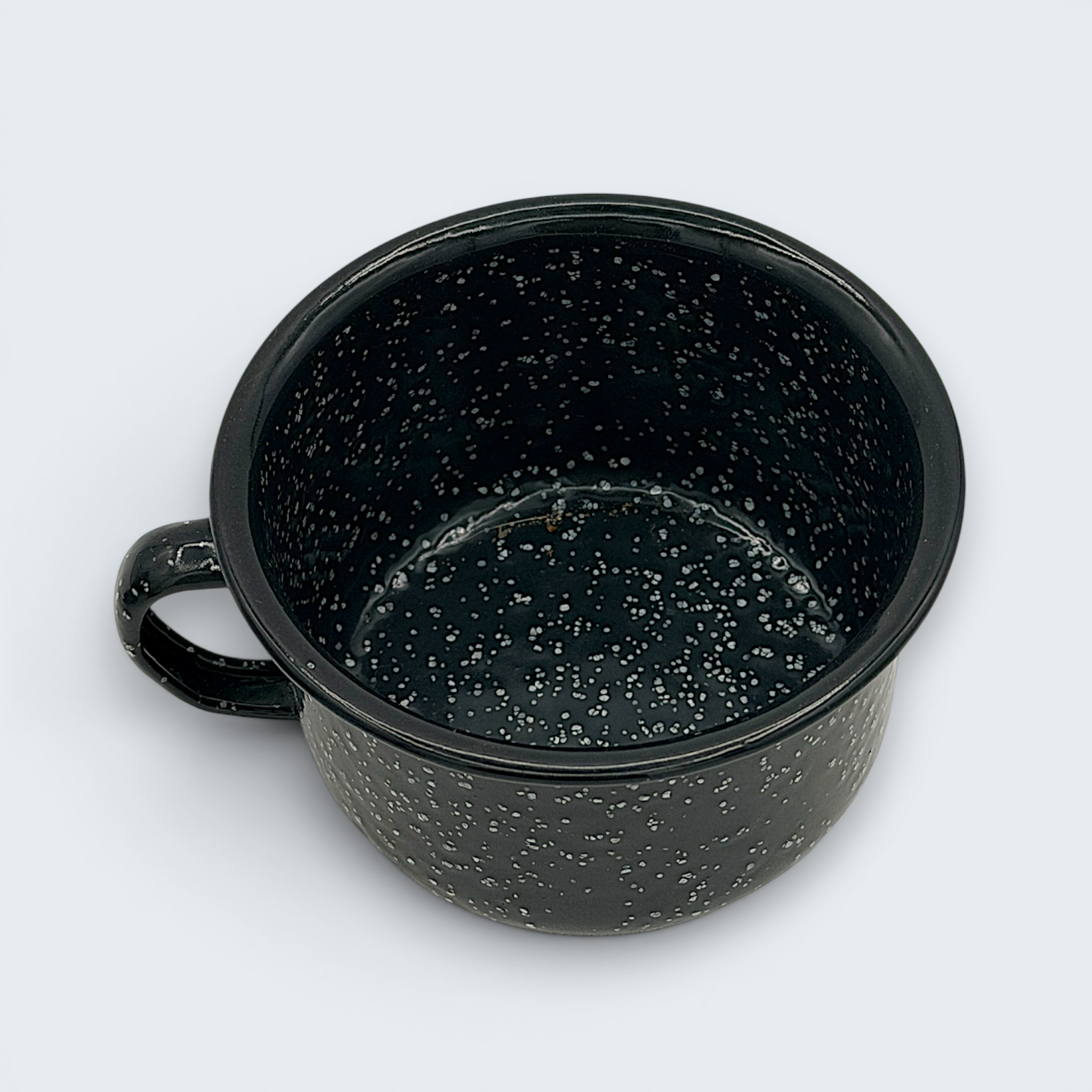 A vintage black enamel cup with white speckles and a single handle, showing a rustic interior with character-building wear at the bottom. - Photo 4