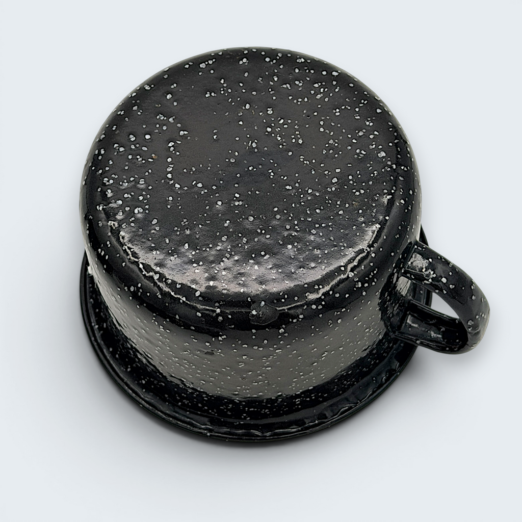 A vintage black enamel cup with white speckles and a single handle, showing a rustic interior with character-building wear at the bottom. - Photo 5