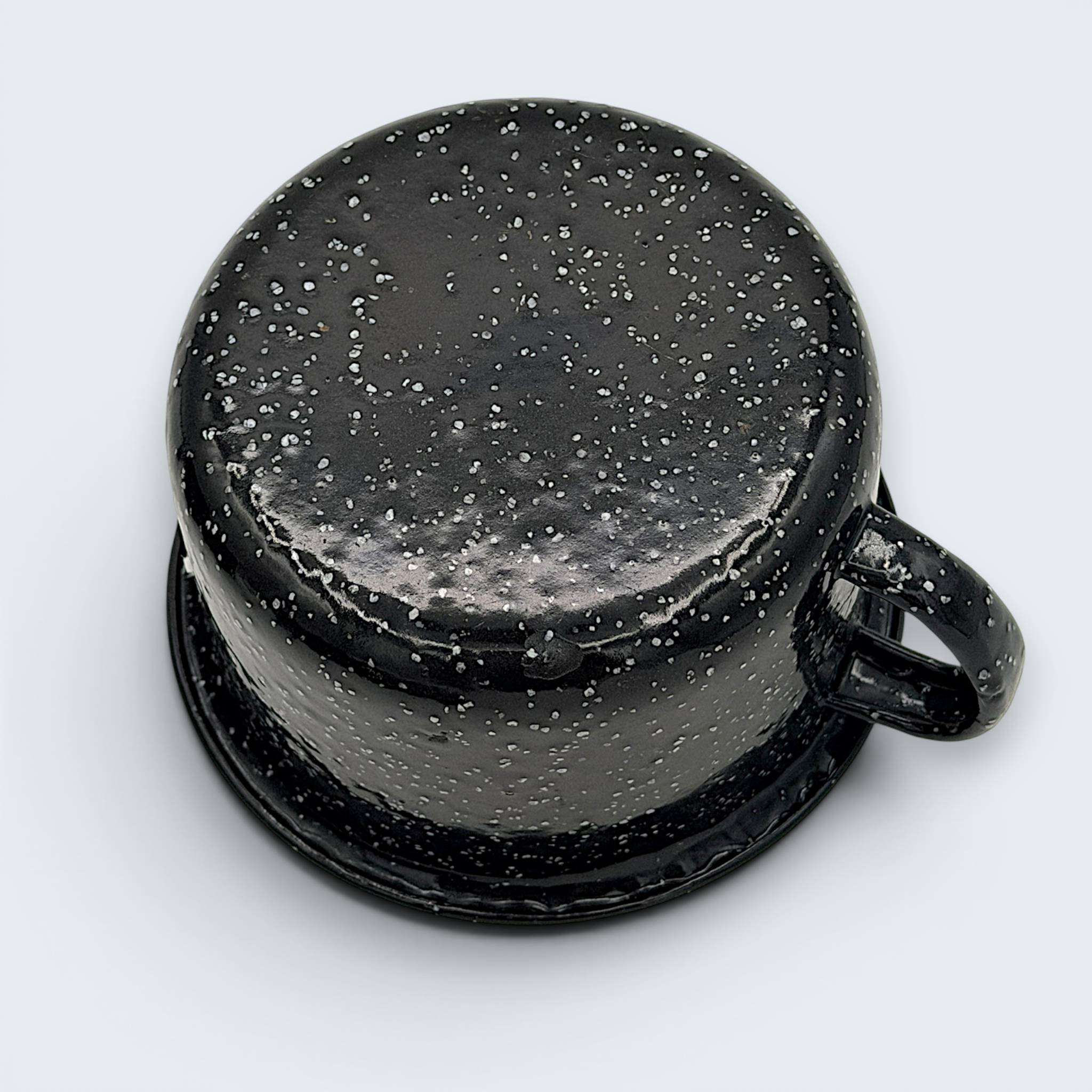 A vintage black enamel cup with white speckles and a single handle, showing a rustic interior with character-building wear at the bottom. - Photo 5