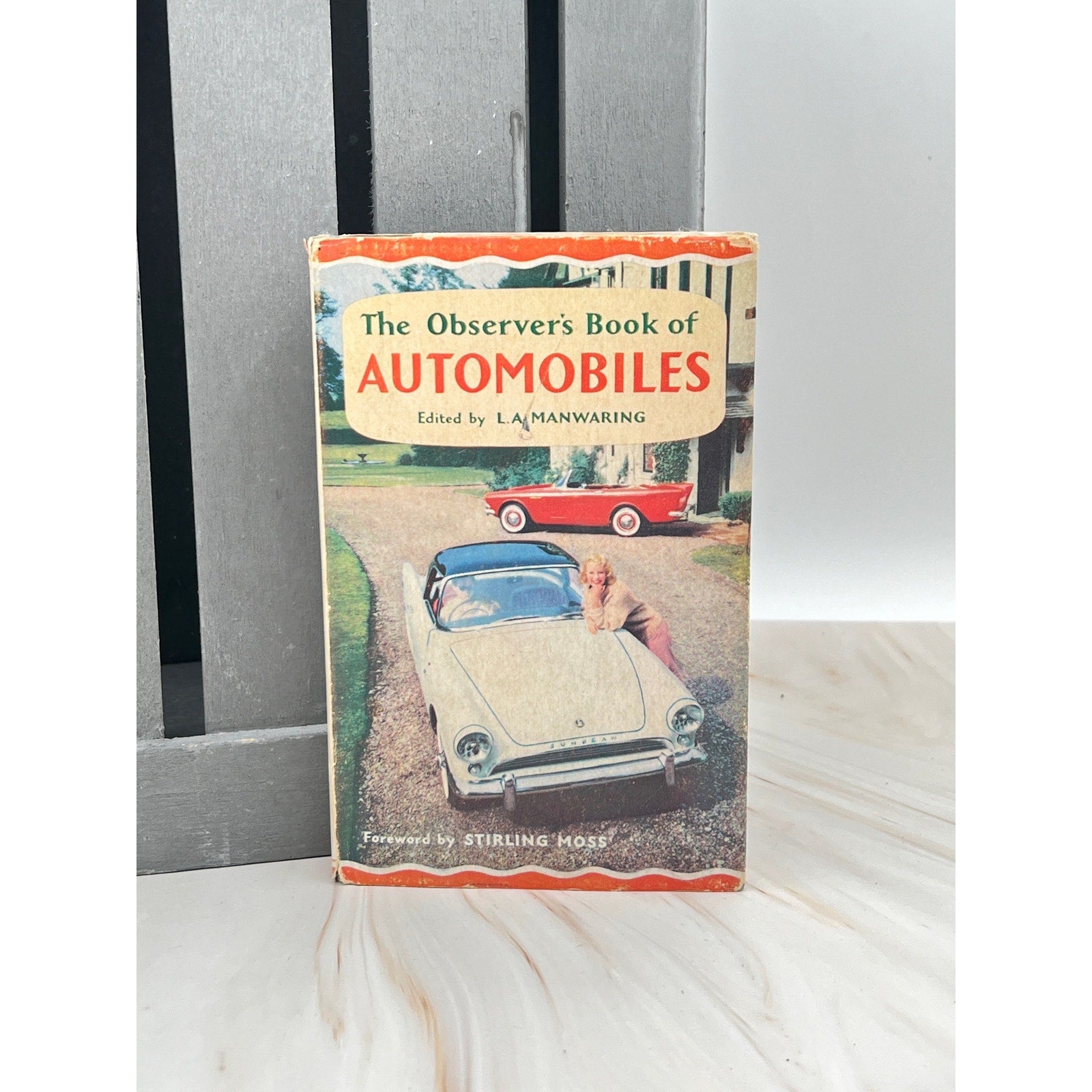 Book titled 'The Observer's Book of Automobiles' on a white surface with a gray background