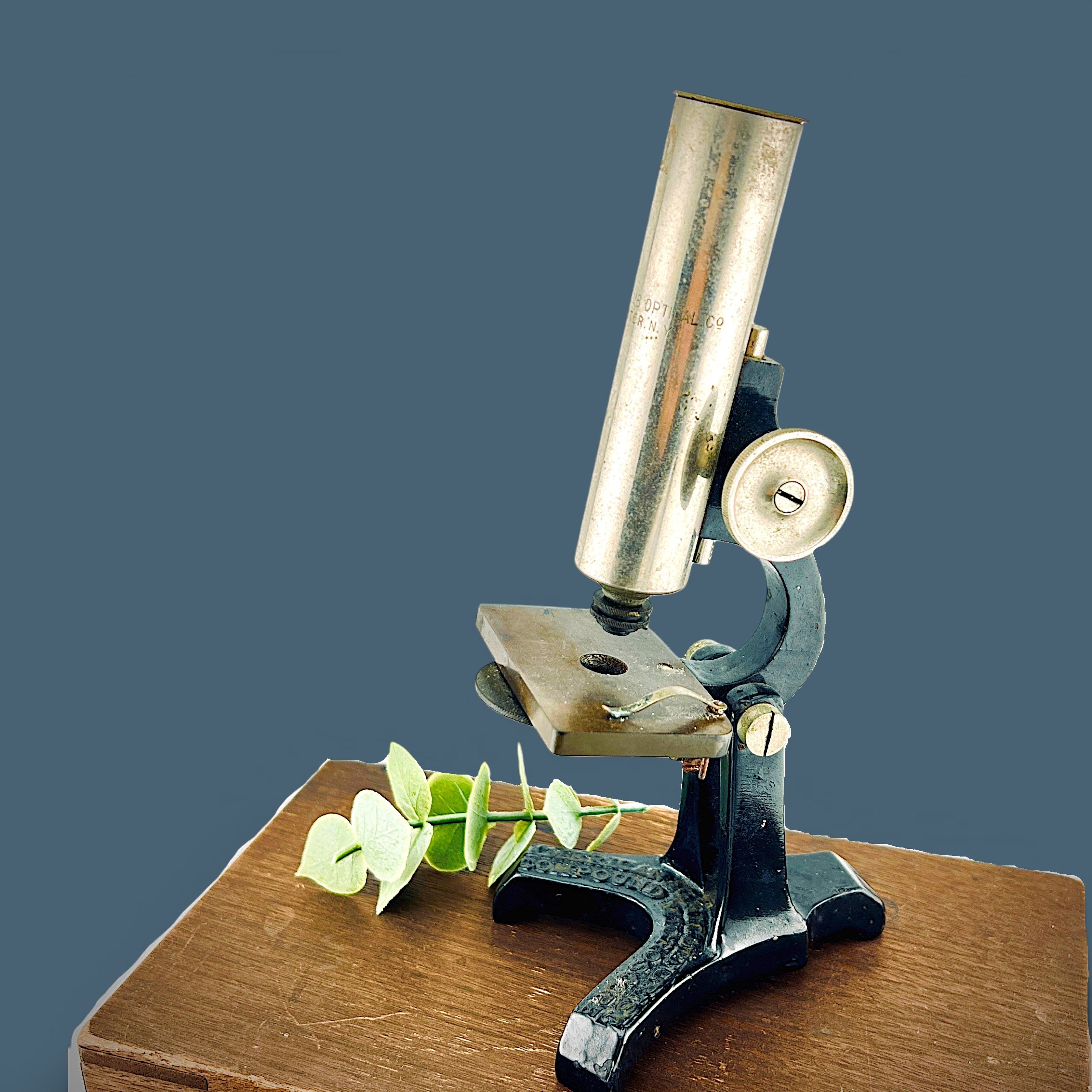 An antique silver-colored steel microscope standing vertically against a solid background, showcasing its classic cylindrical body tube, focus adjustment wheels, and sturdy black metal base. - Photo 1