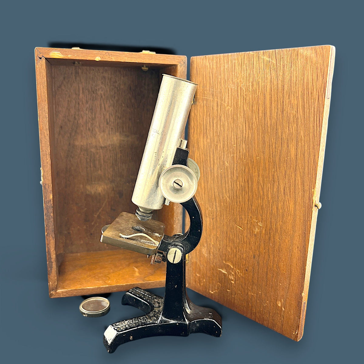 An antique silver-colored steel microscope standing vertically against a solid background, showcasing its classic cylindrical body tube, focus adjustment wheels, and sturdy black metal base. - Photo 2
