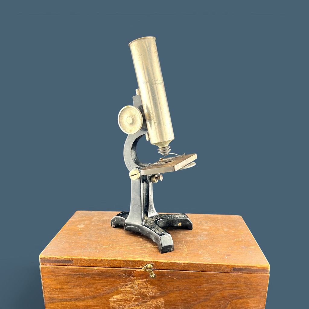 An antique silver-colored steel microscope standing vertically against a solid background, showcasing its classic cylindrical body tube, focus adjustment wheels, and sturdy black metal base. - Photo 3