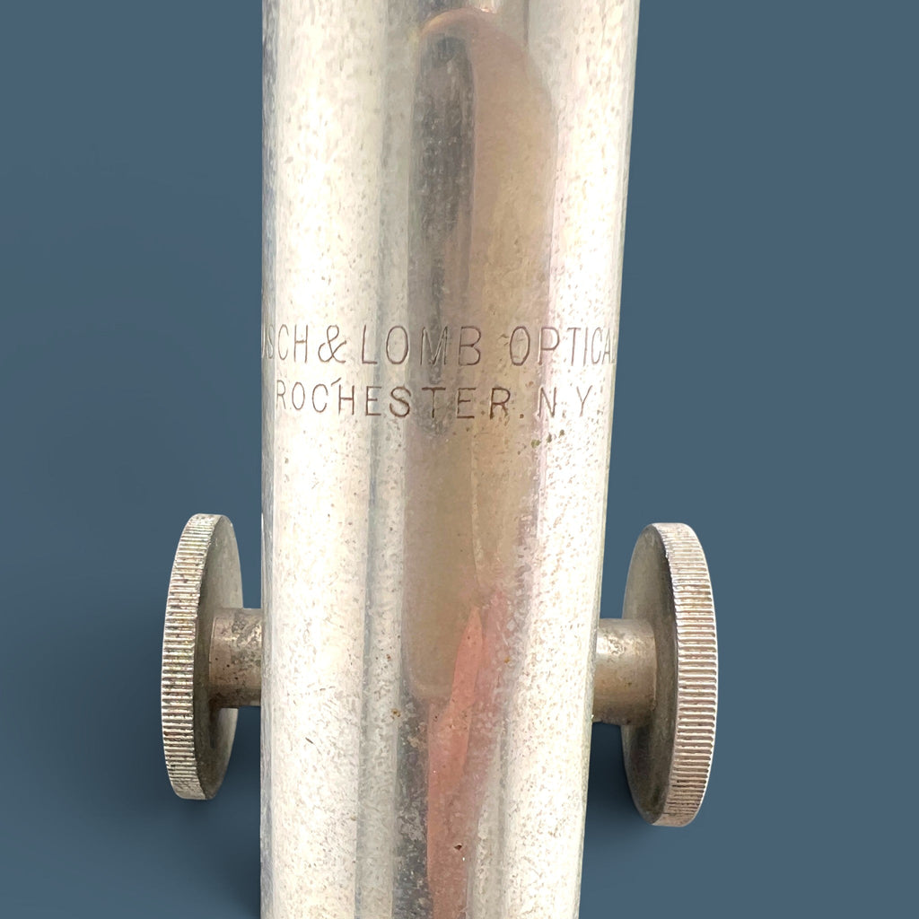 An antique silver-colored steel microscope standing vertically against a solid background, showcasing its classic cylindrical body tube, focus adjustment wheels, and sturdy black metal base. - Photo 5