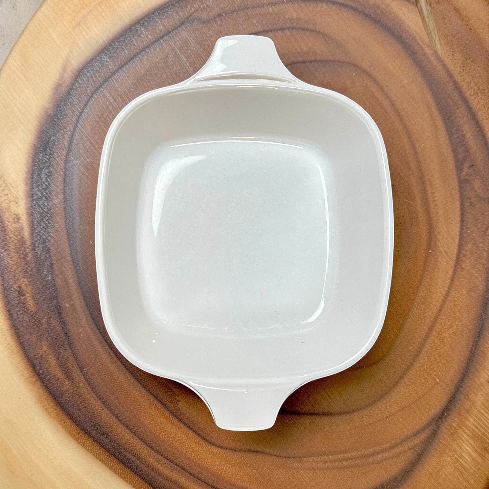 A square-shaped white Corning Ware petite casserole dish with lug handles, resting on a rustic wood slice background. - Photo 4